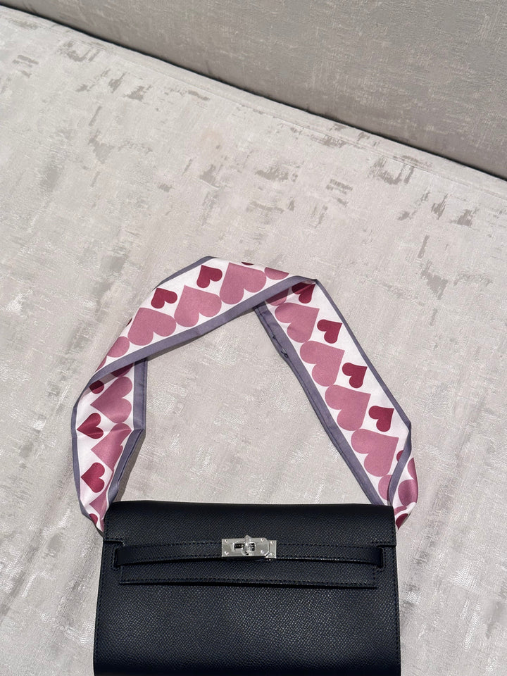 Black handbag with a pink heart-patterned strap on a gray surface