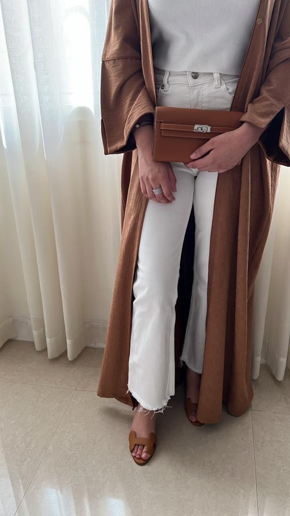 Person wearing a long brown coat holding a brown handbag indoors.