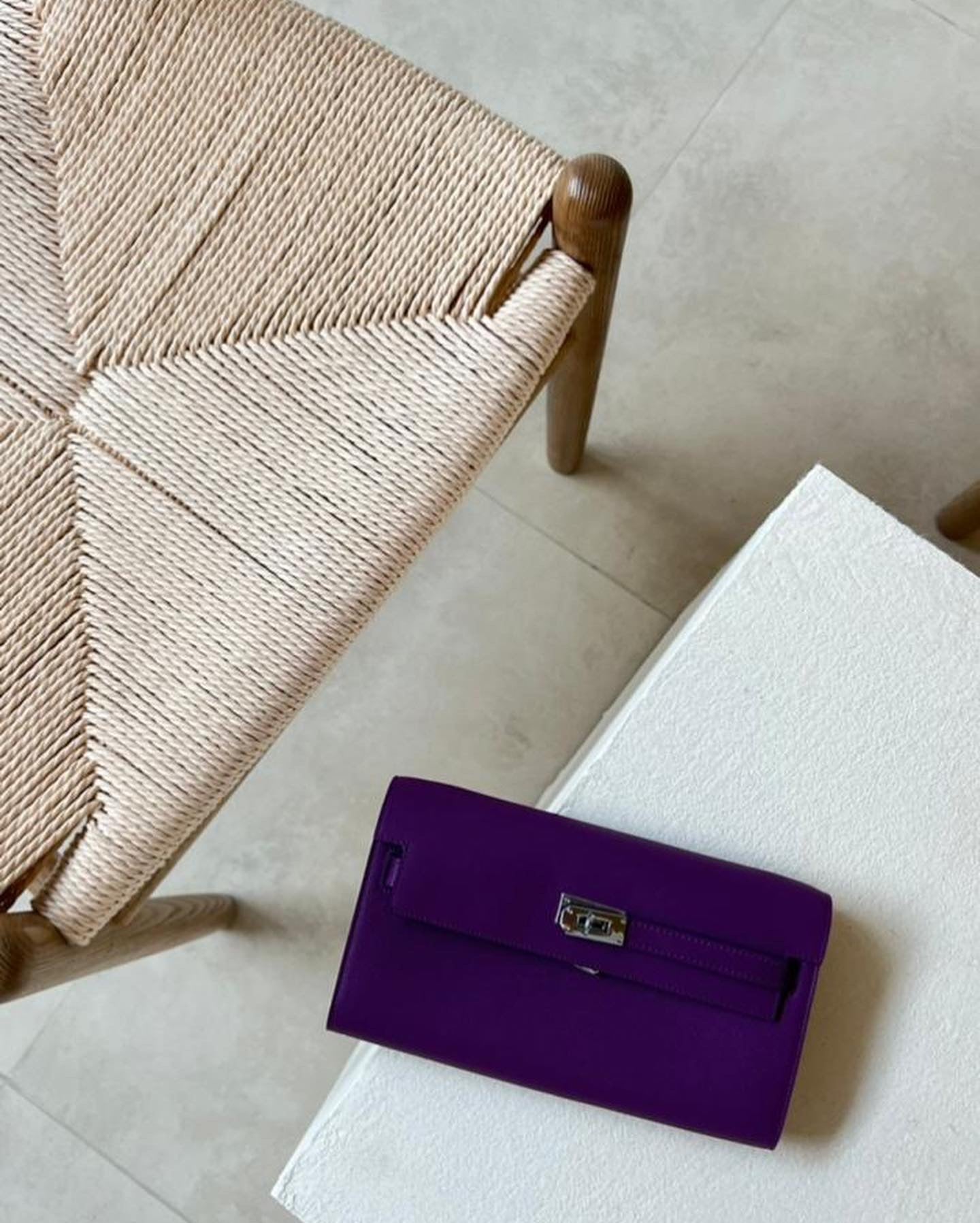 Purple handbag on a white surface next to a woven chair