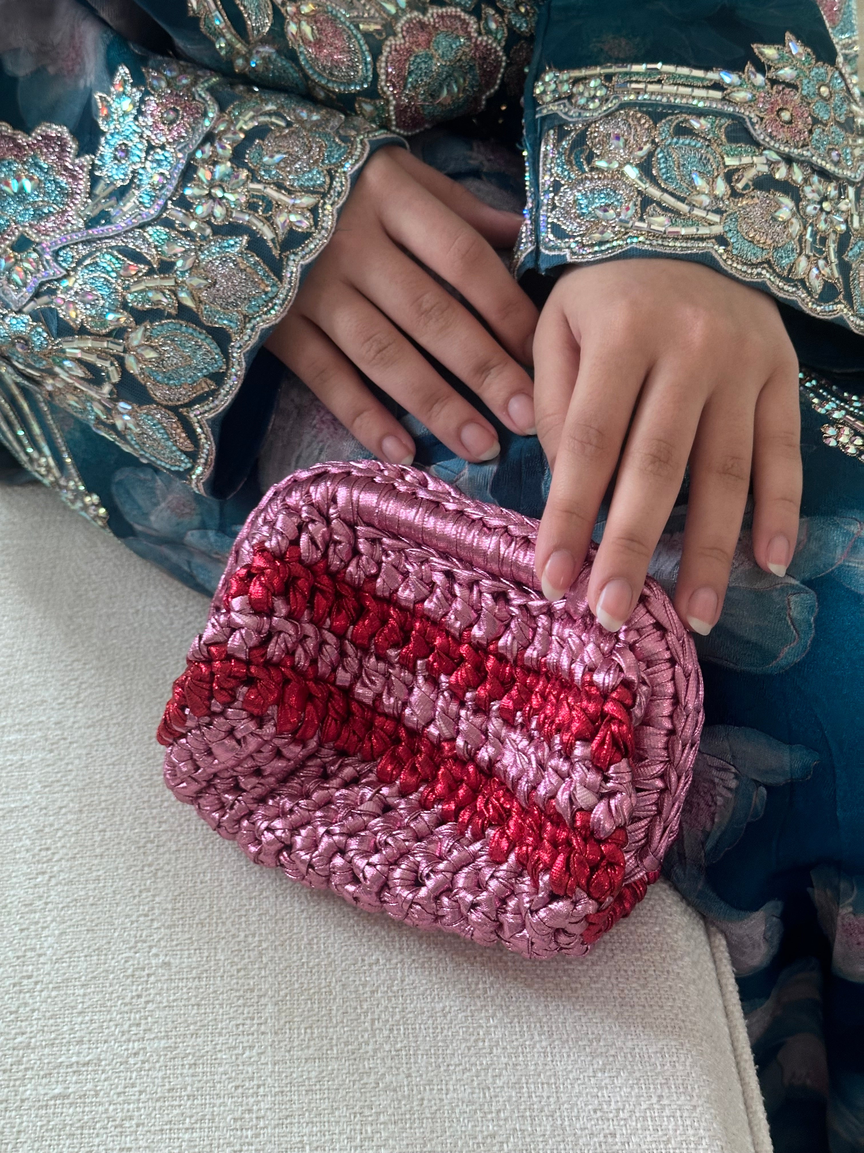 Person holding a pink and red striped pouch with embroidered clothing in the background