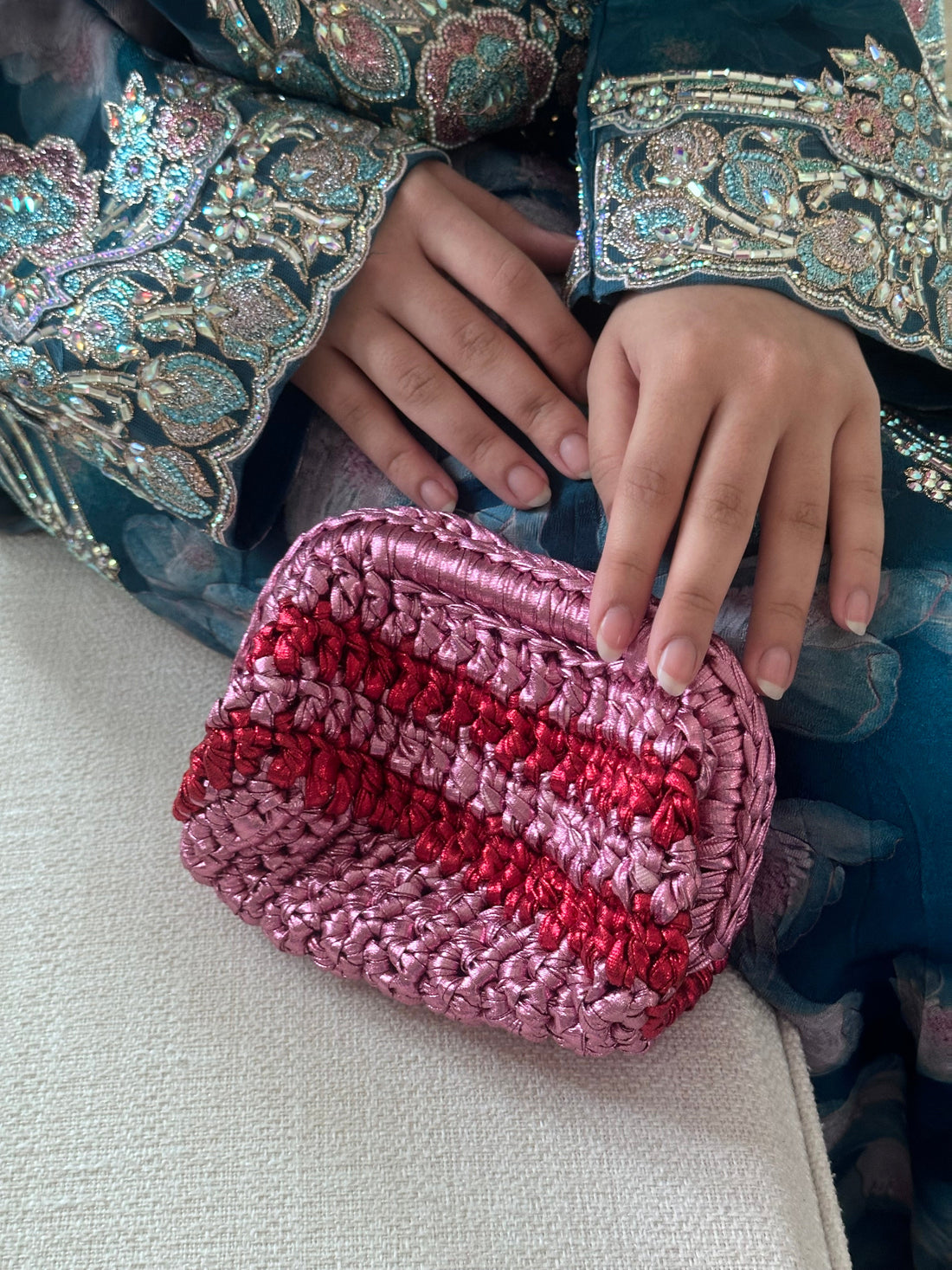 Person holding a pink and red striped pouch with embroidered clothing in the background