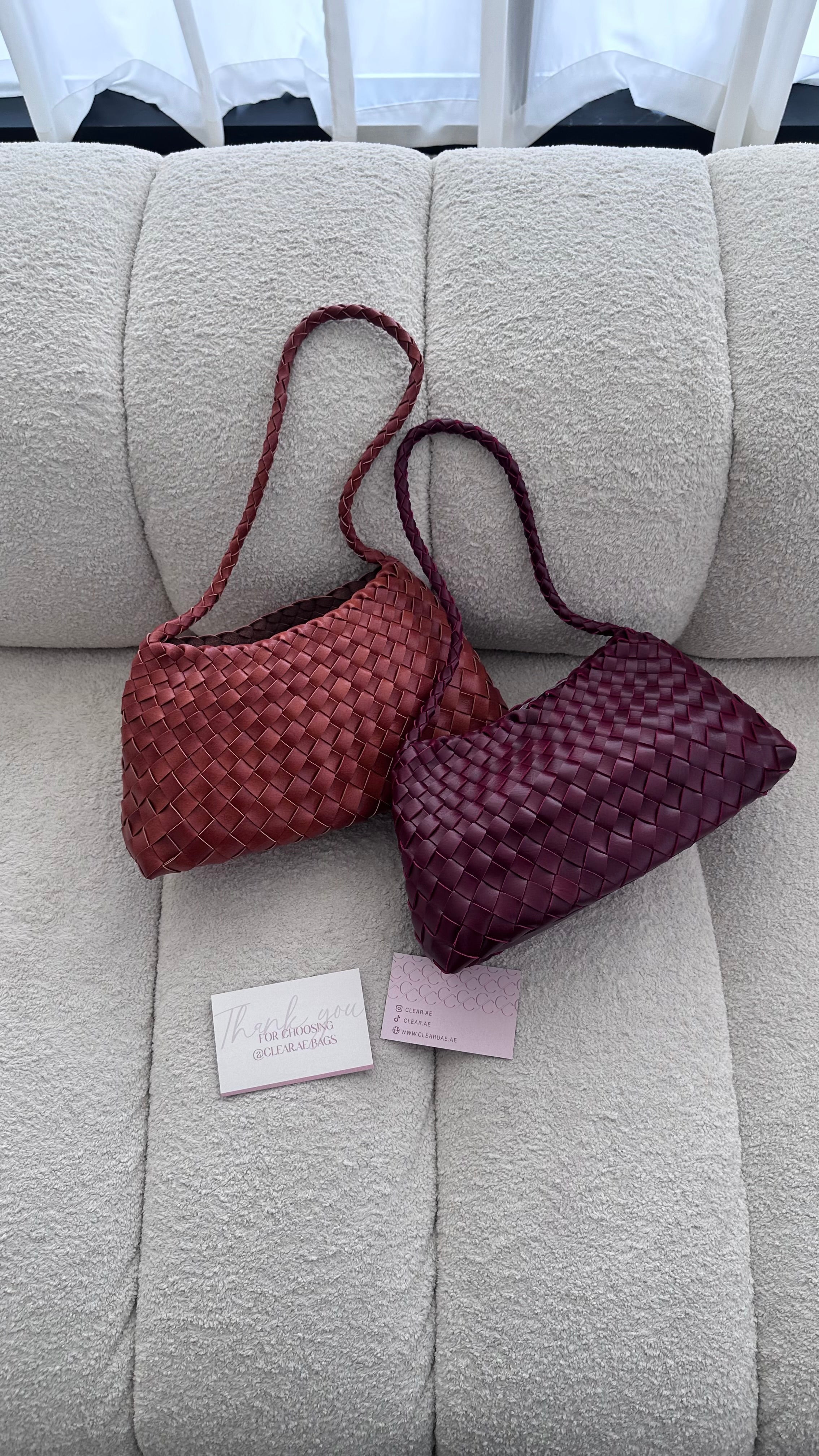 Two woven handbags on a light gray couch with a visible brand tag.