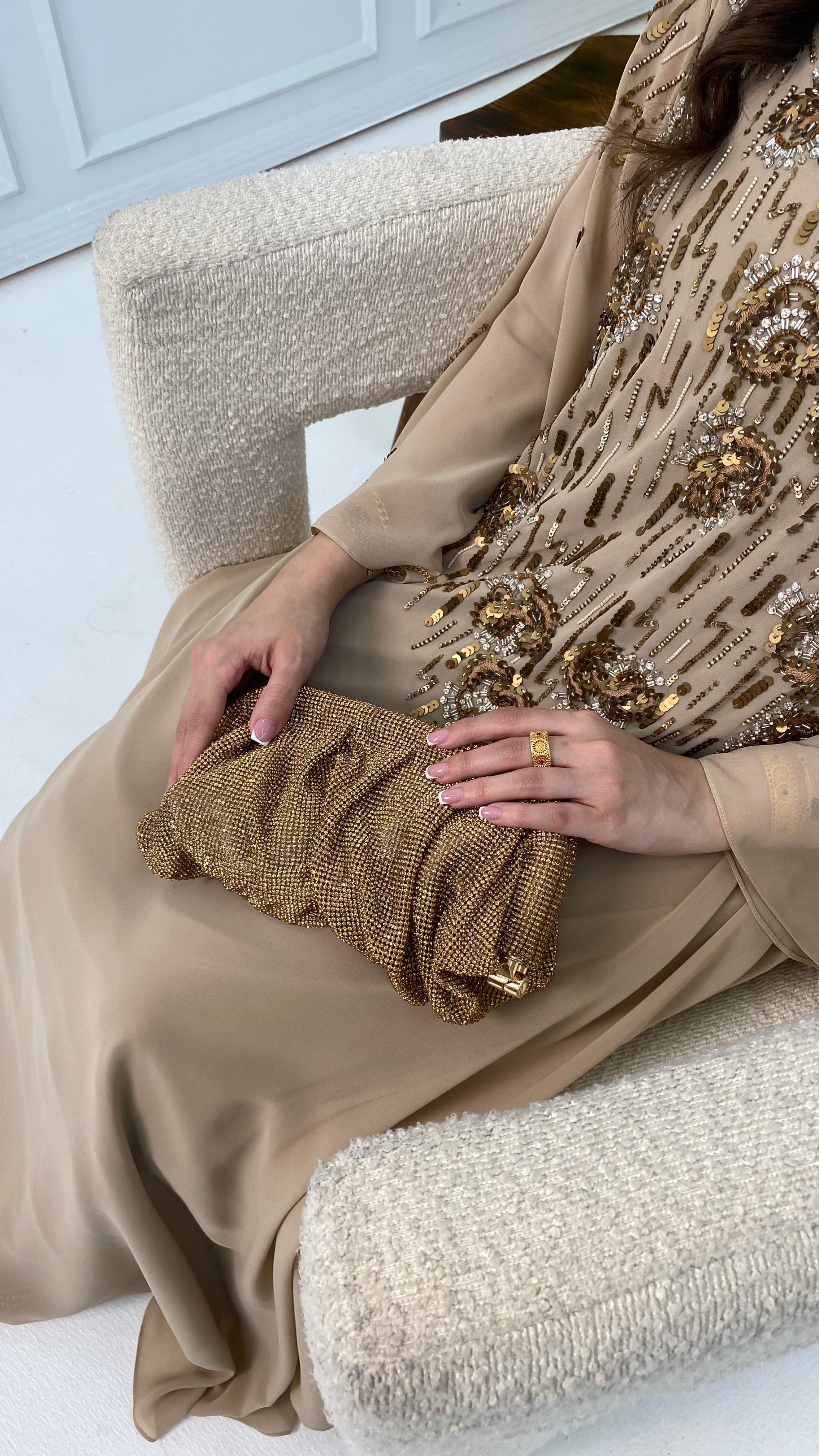Person holding a gold clutch bag with a neutral-toned outfit on a light background