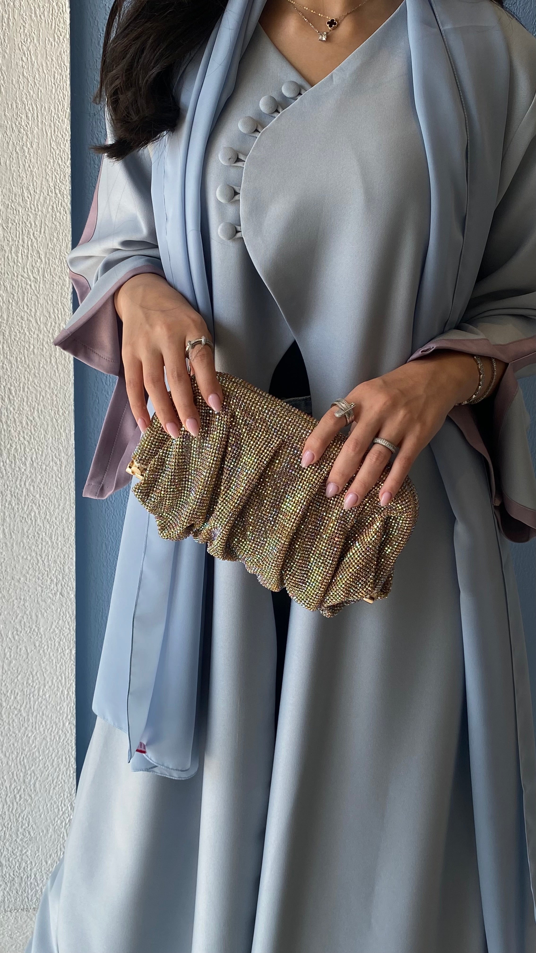 Woman holding a gold clutch wearing a light blue dress with a matching shawl.