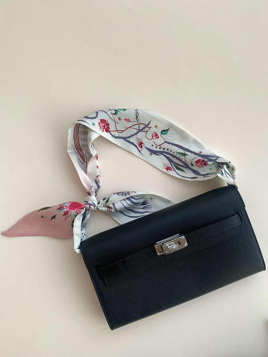 Black handbag with a floral scarf draped over it on a light background