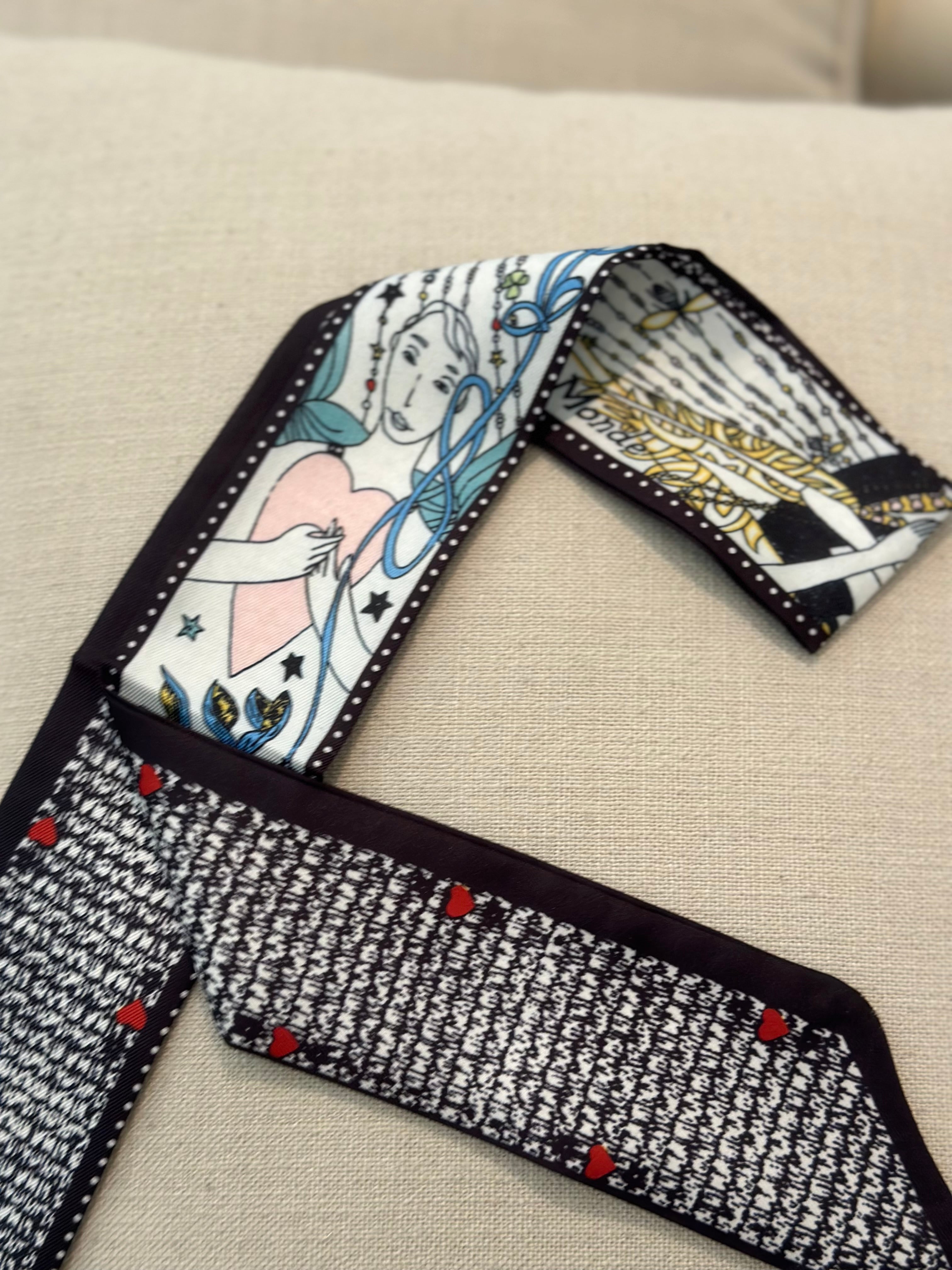 This image displays an elegant scarf with a dual-sided design, laid out on a neutral background to emphasize its patterns and colors. The scarf features a detailed, artistic illustration on one side, portraying a classical scene with characters and decorative elements in a vibrant color palette.