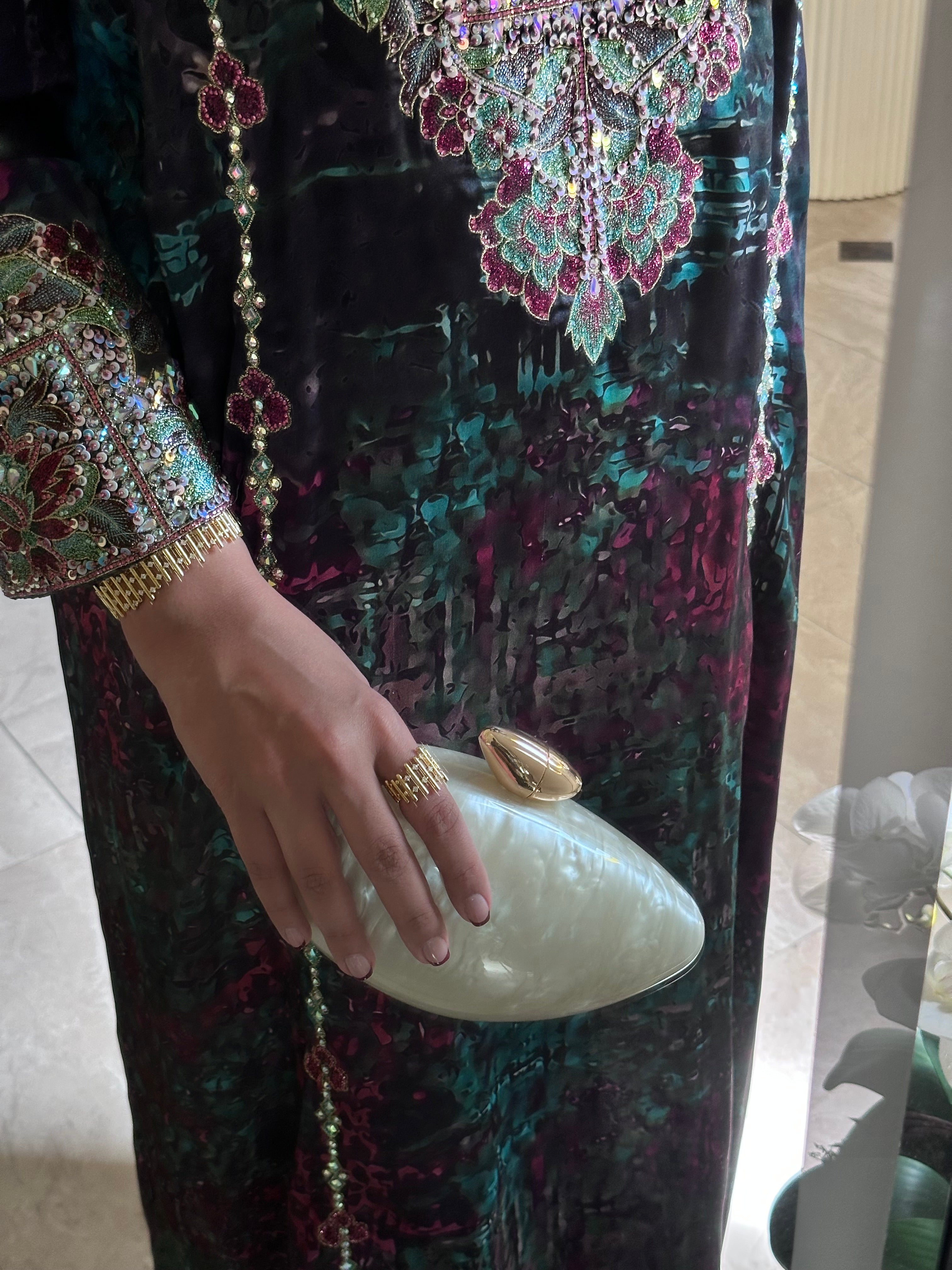 Person wearing a colorful embroidered outfit holding a white clutch.