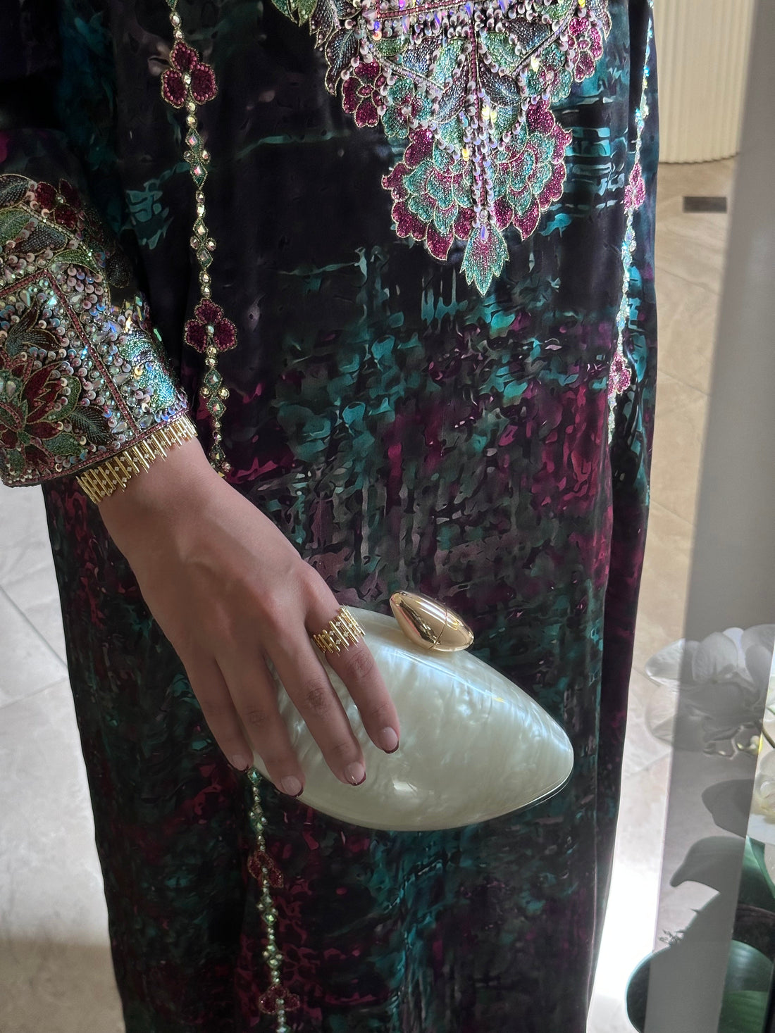 Person wearing a colorful embroidered outfit holding a white clutch.