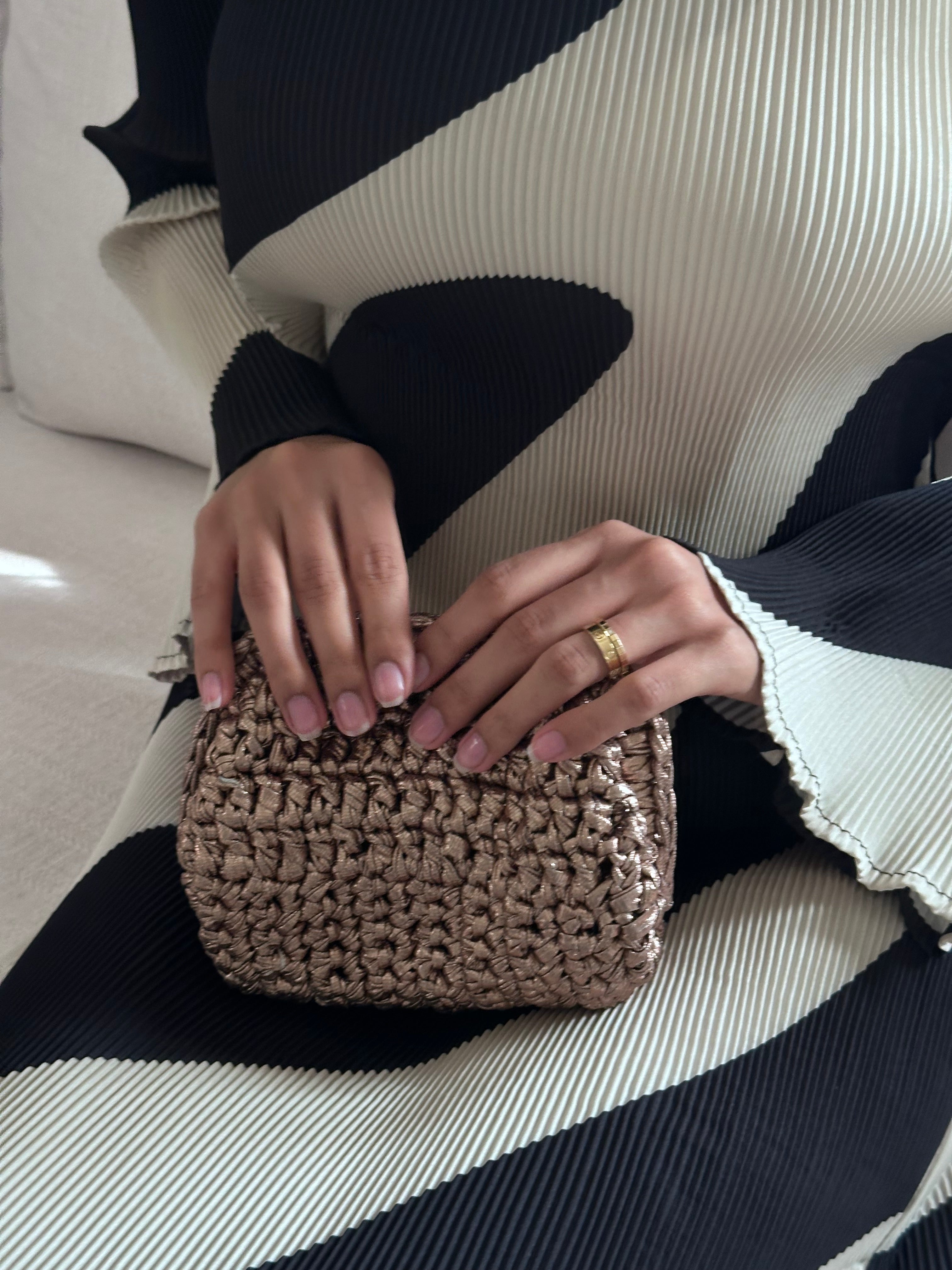 Person holding a woven handbag with a black and white patterned sweater