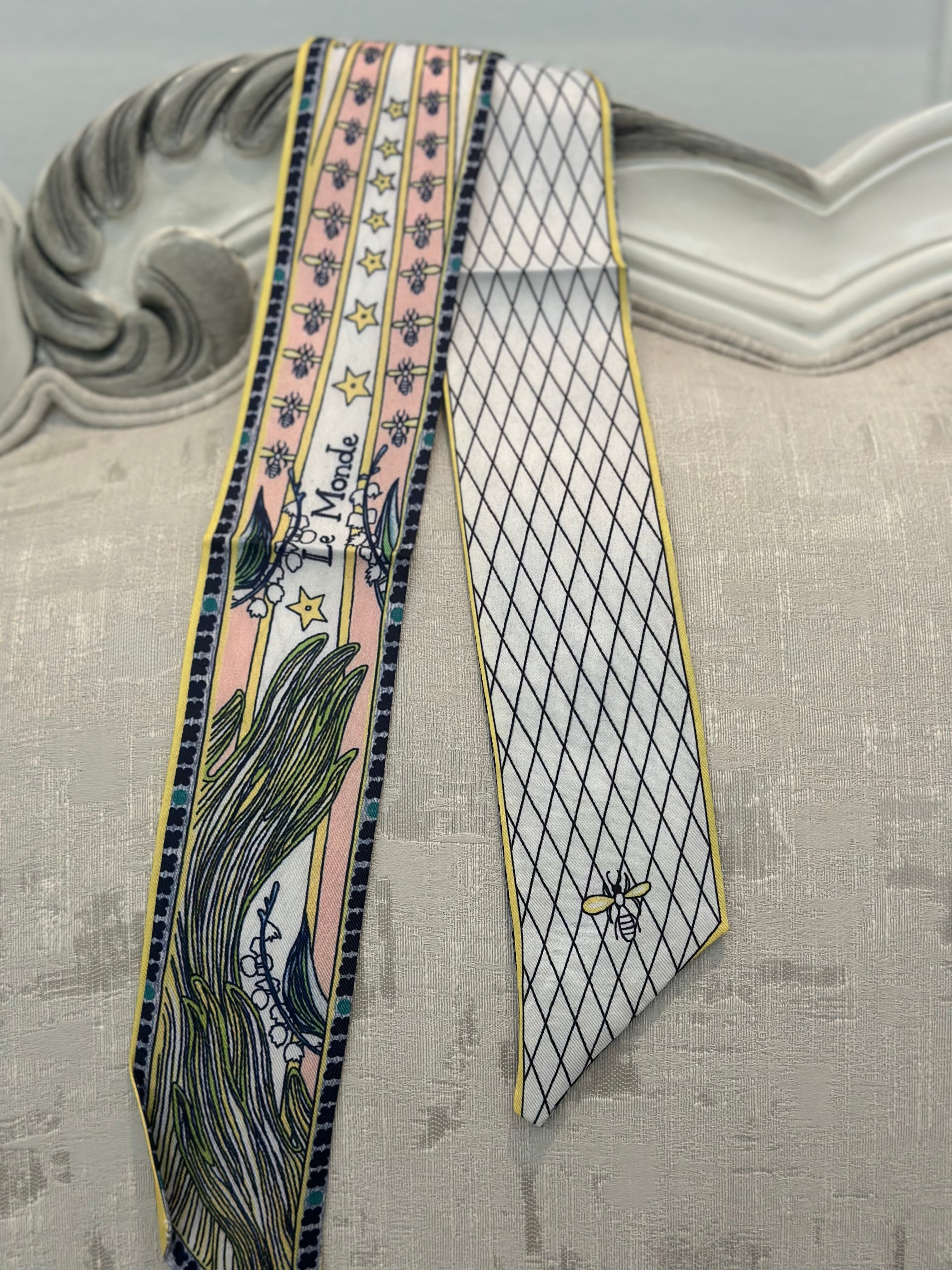 A patterned necktie with a floral design and geometric motifs, predominantly in shades of pink, white, and gold, with a clip on the top.