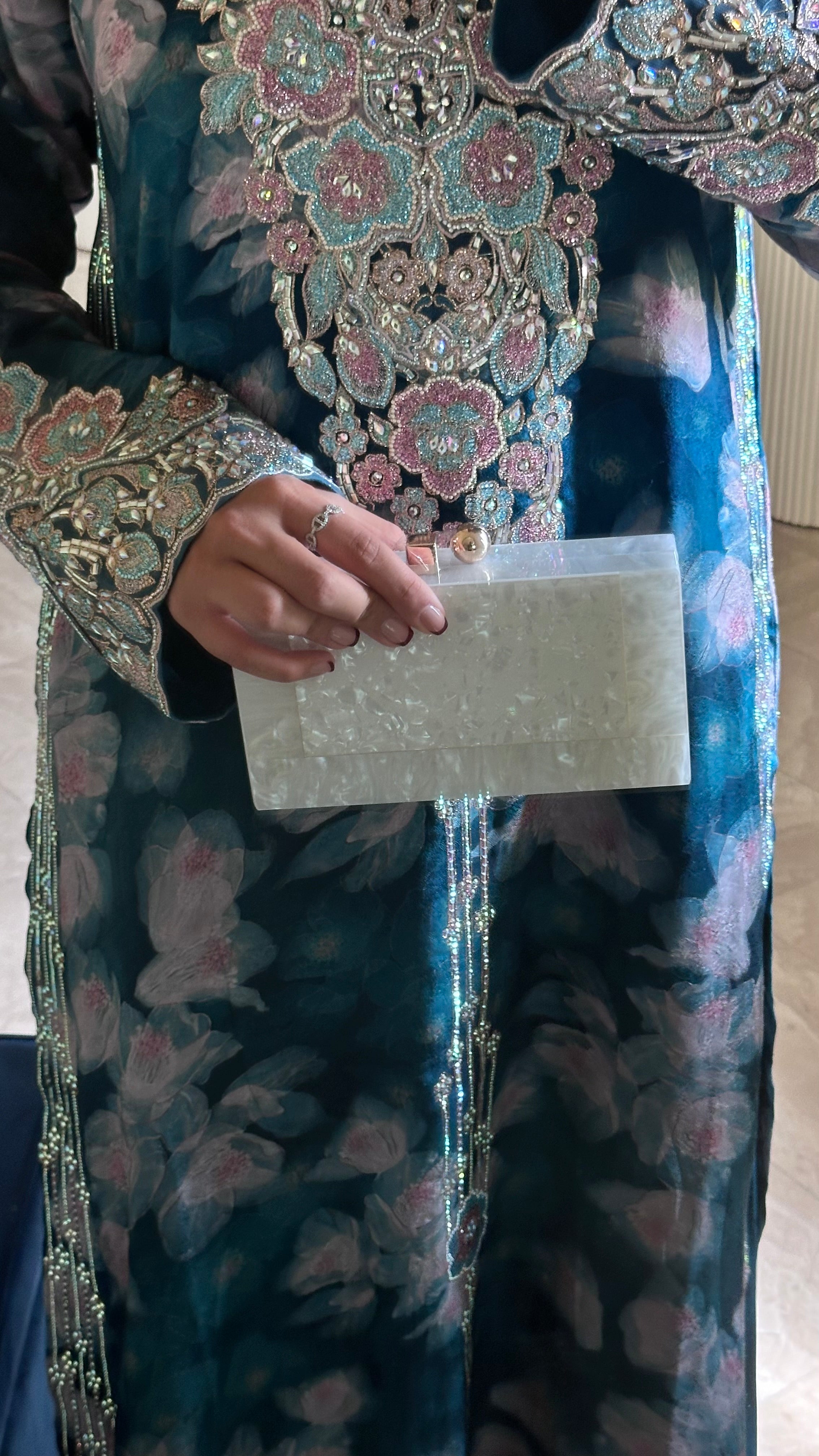 Person wearing a traditional embroidered garment holding a white card.