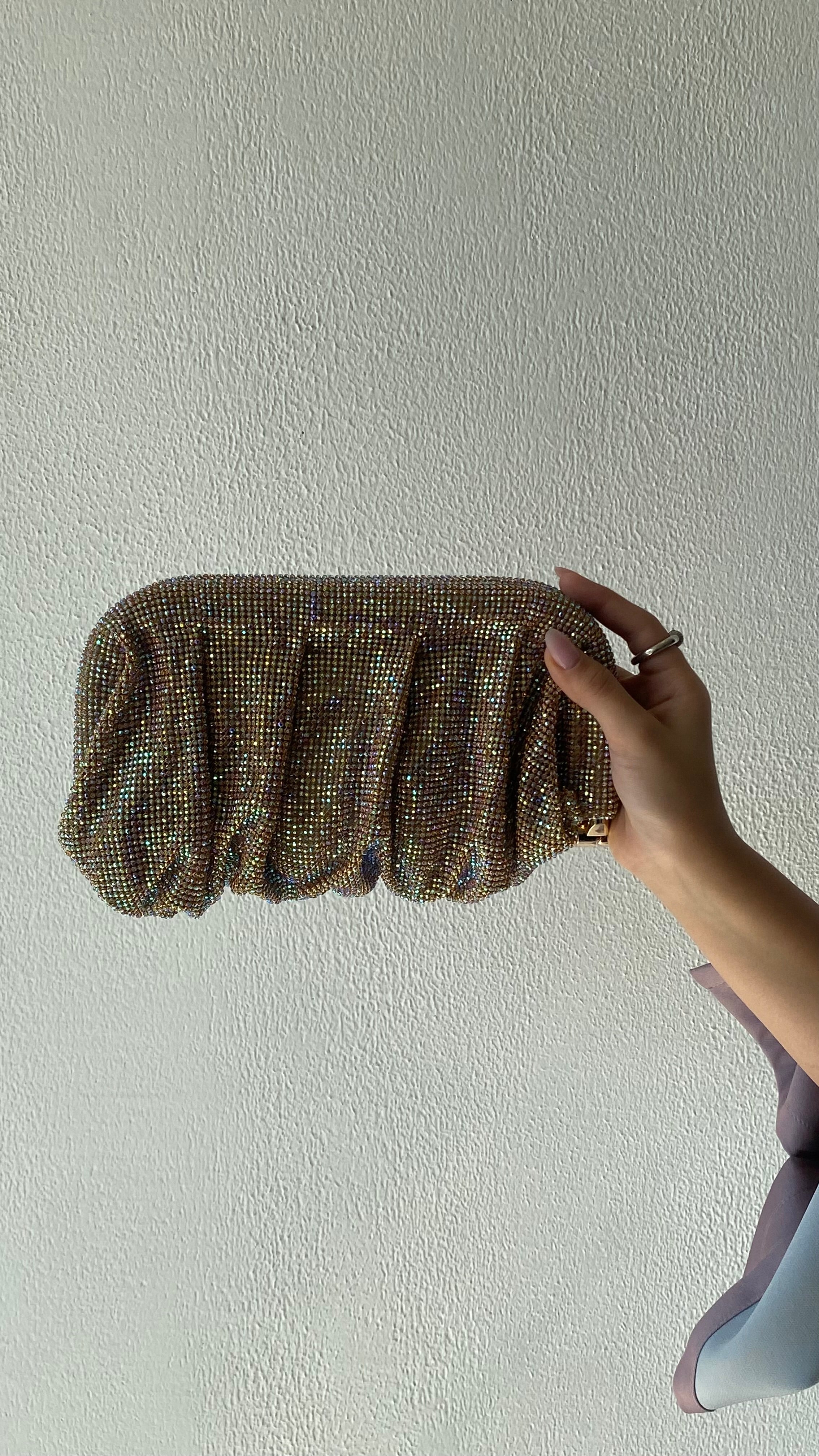 Gold beaded clutch held by a hand against a plain background