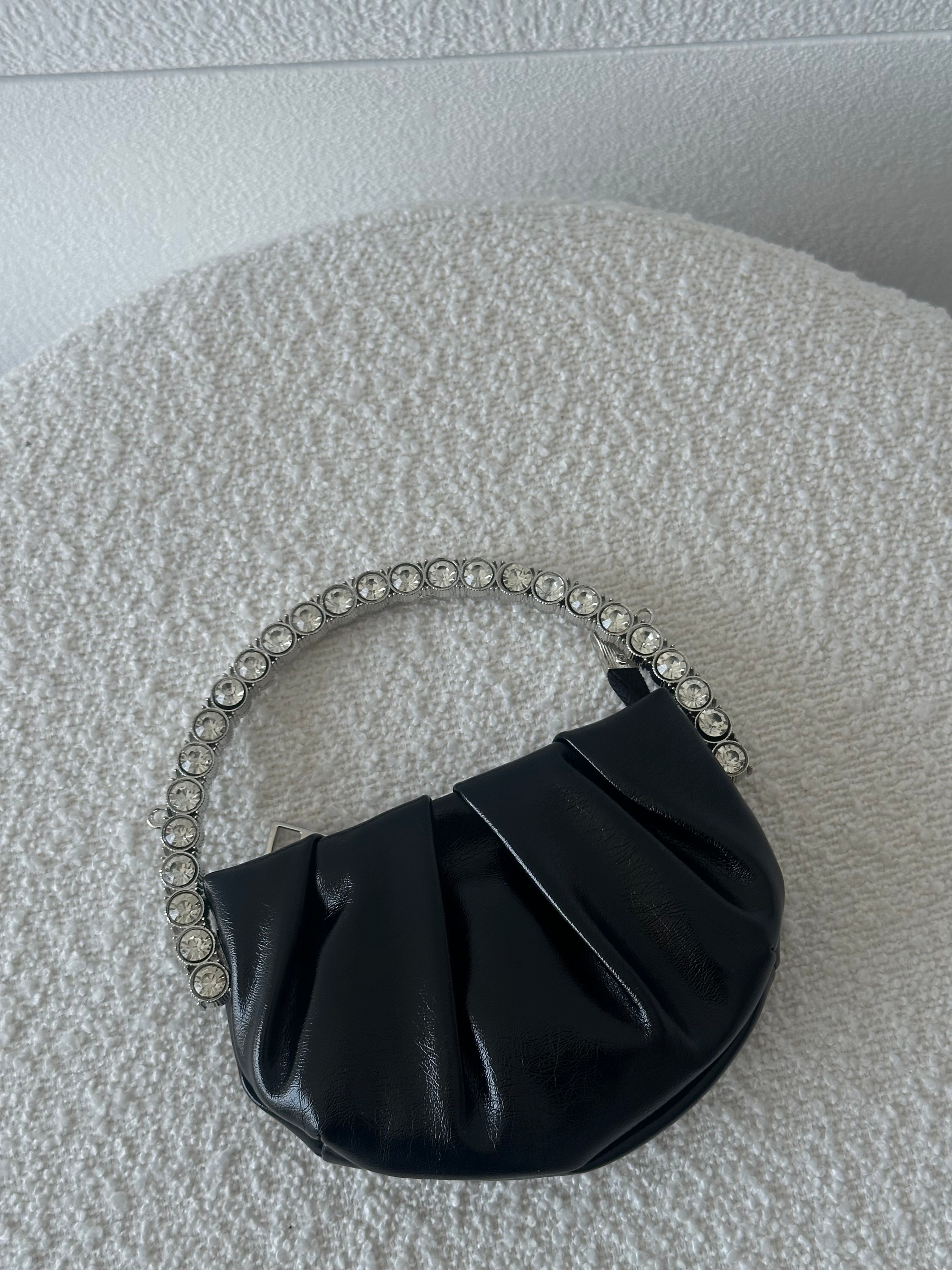 A small black handbag with a chain handle laid out on a textured surface.