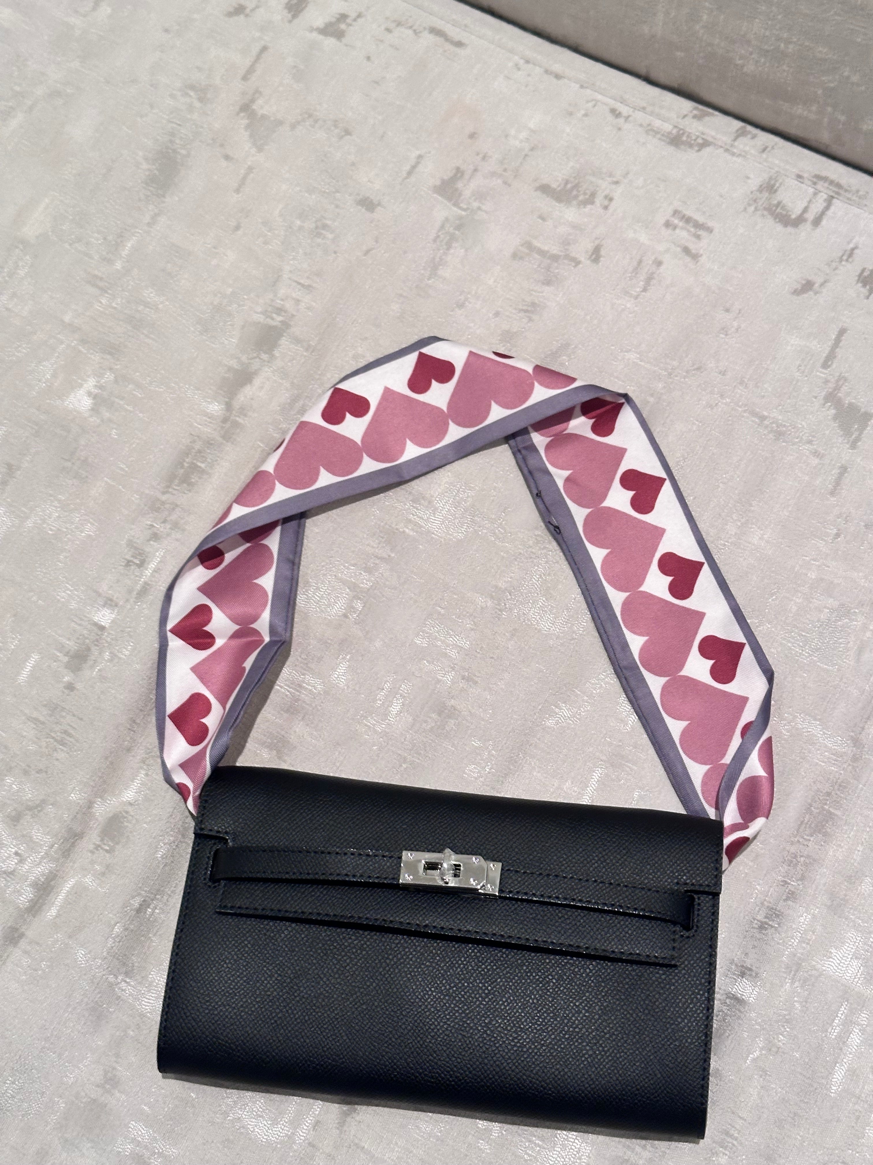 Black handbag with a pink heart-patterned strap on a concrete surface