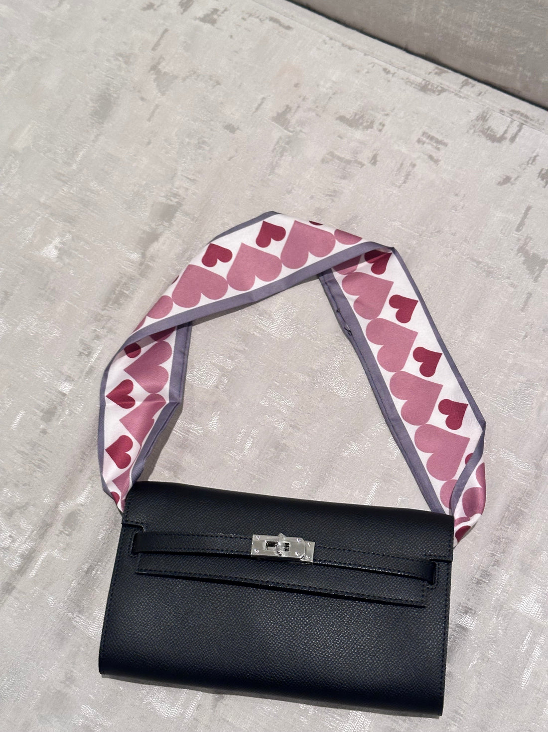 Black handbag with a pink heart-patterned strap on a concrete surface