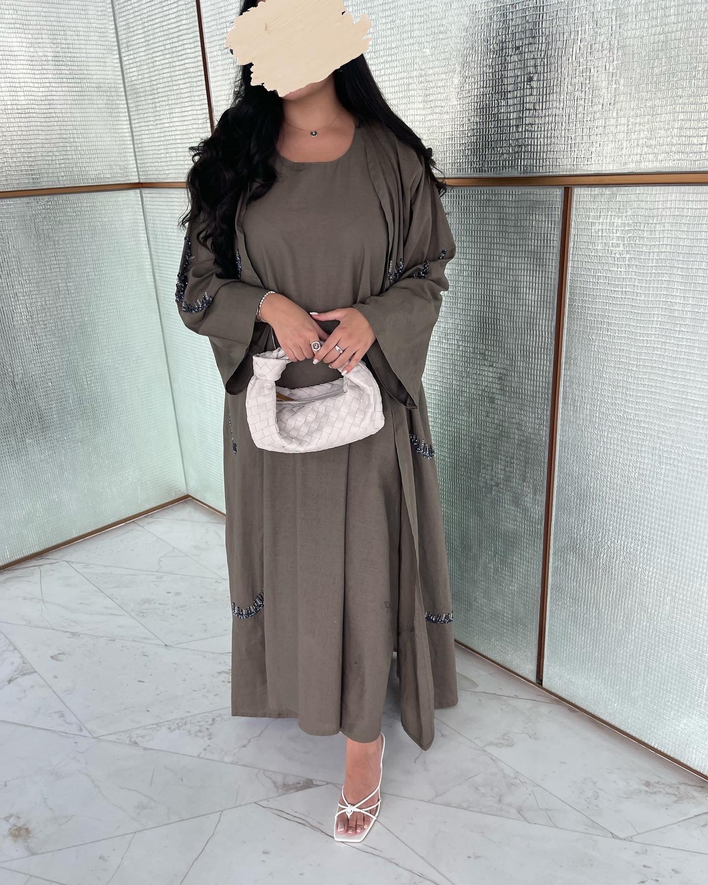 Woman wearing a long olive green dress with a white handbag indoors.