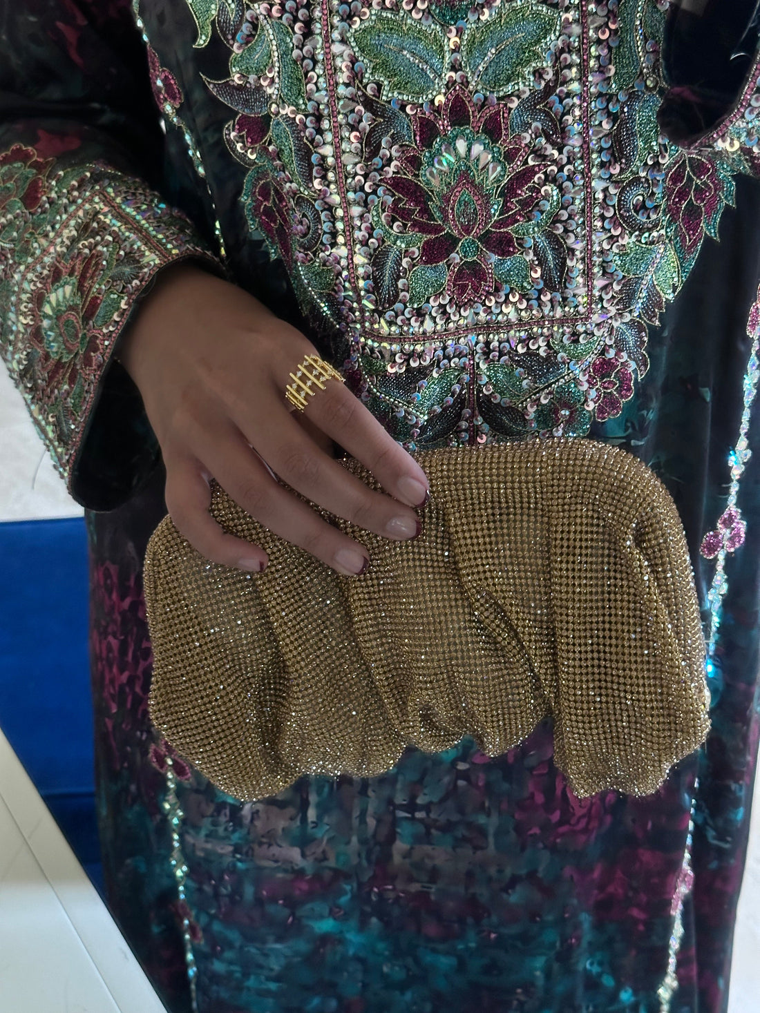 Gold beaded gloves held by a person wearing a colorful, patterned garment.