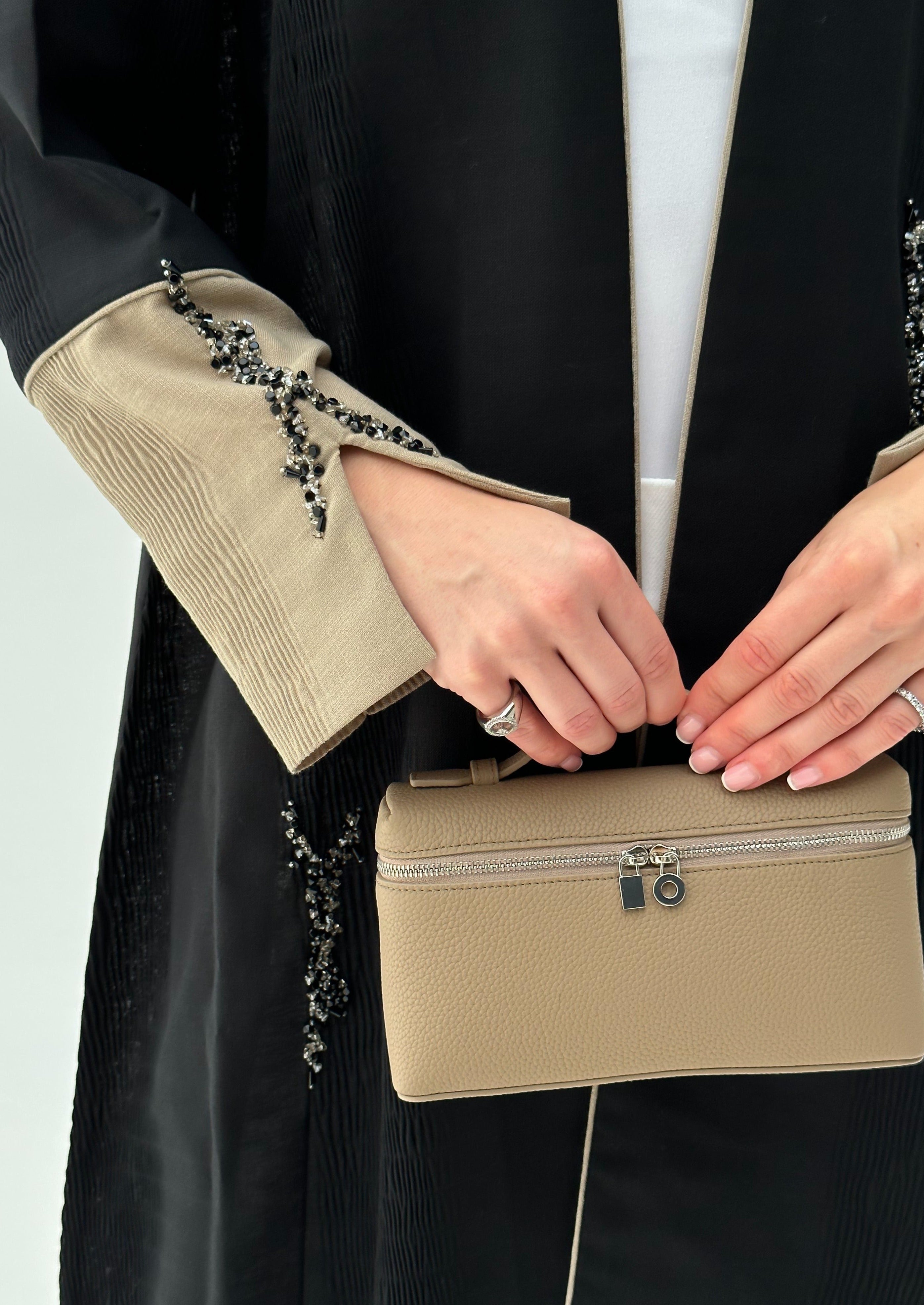 A person wearing a black and beige outfit holding a beige handbag with a strap.