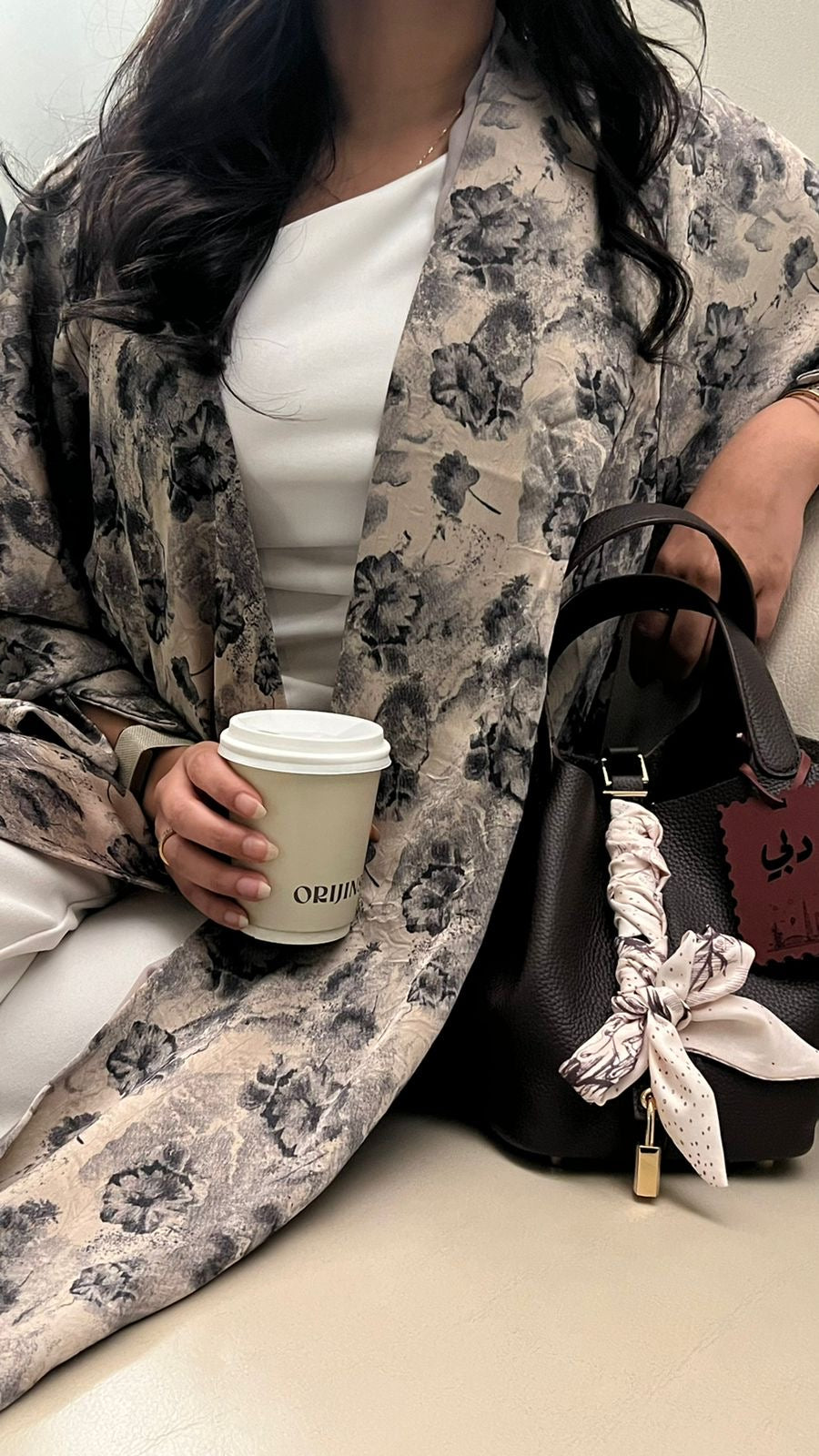 Person holding a coffee cup and a black handbag with floral details.