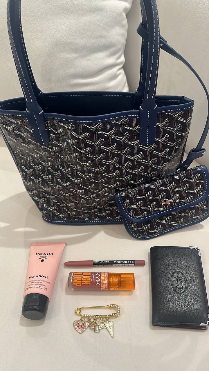 Blue patterned handbag with Prada lotion, makeup items, and a wallet on a white surface