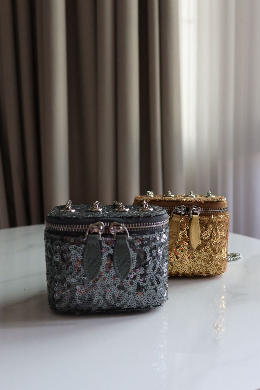 Two decorative bags on a surface with a curtain background