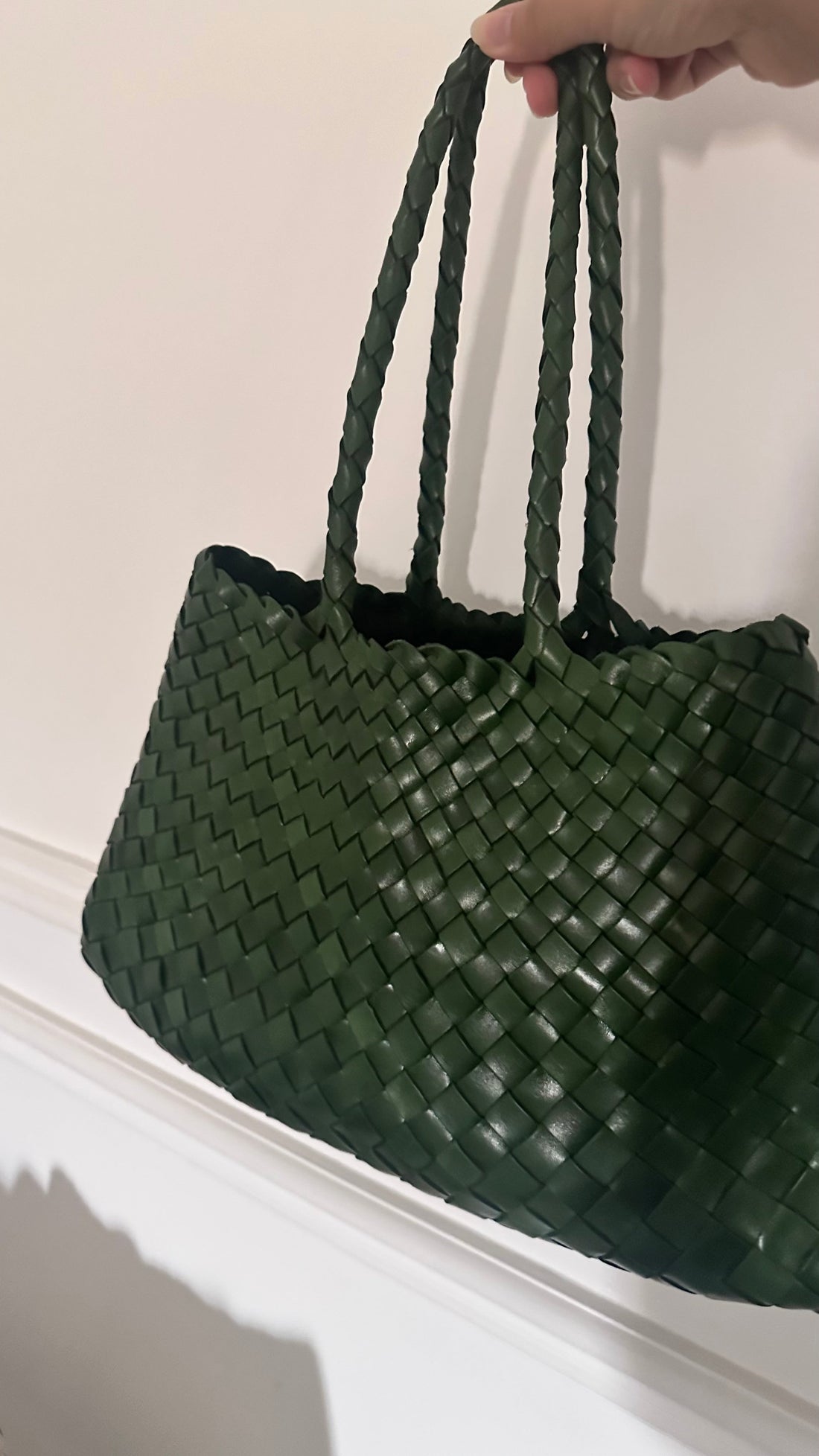 Green woven handbag held by a hand against a plain background