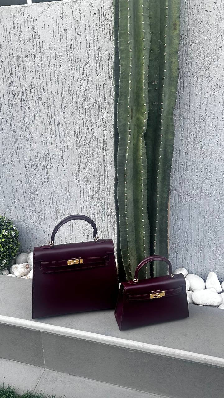 Two burgundy handbags on a ledge with a cactus and decorative stones in the background.