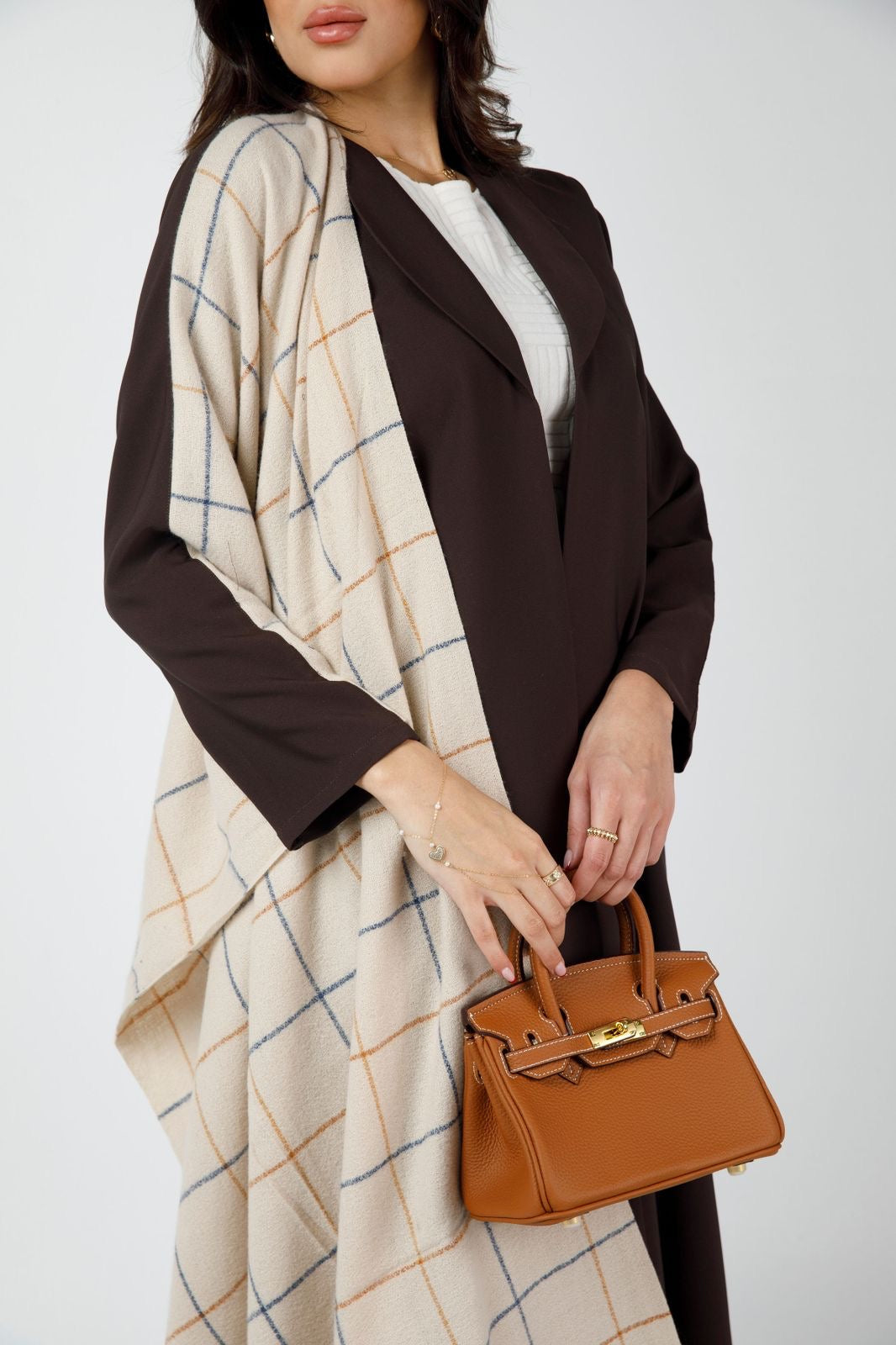 A woman wearing a brown checkered coat with a long strap carrying a small brown handbag with a checkered pattern.