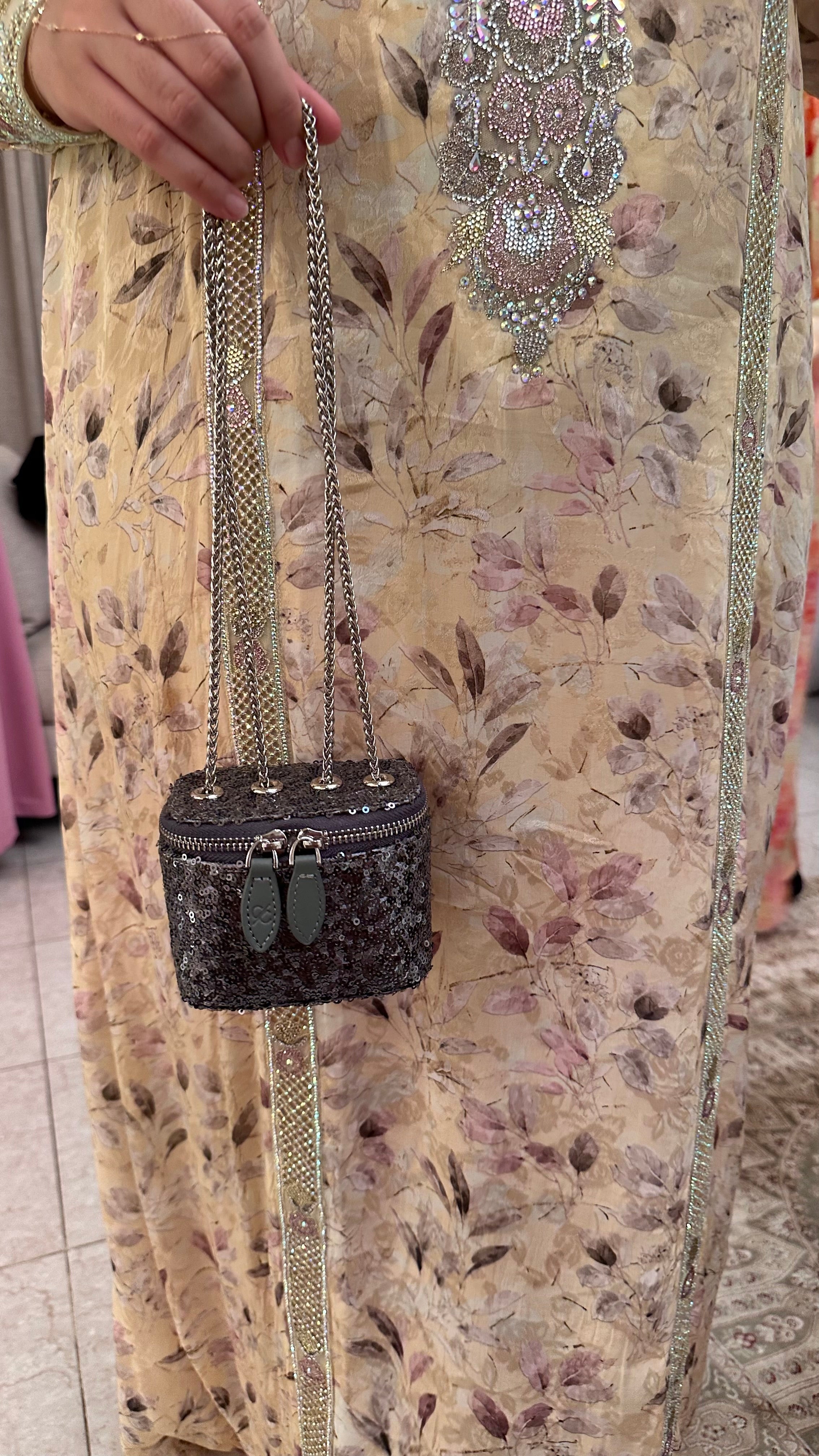 Black glittery handbag with a chain strap held by a person wearing a patterned dress.