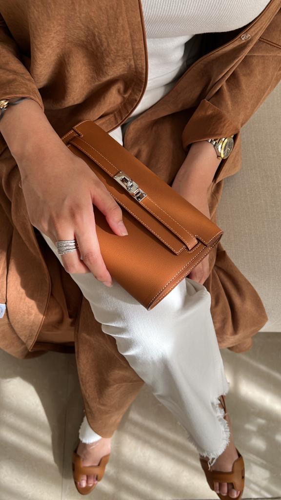 Person holding a brown clutch bag with a neutral background