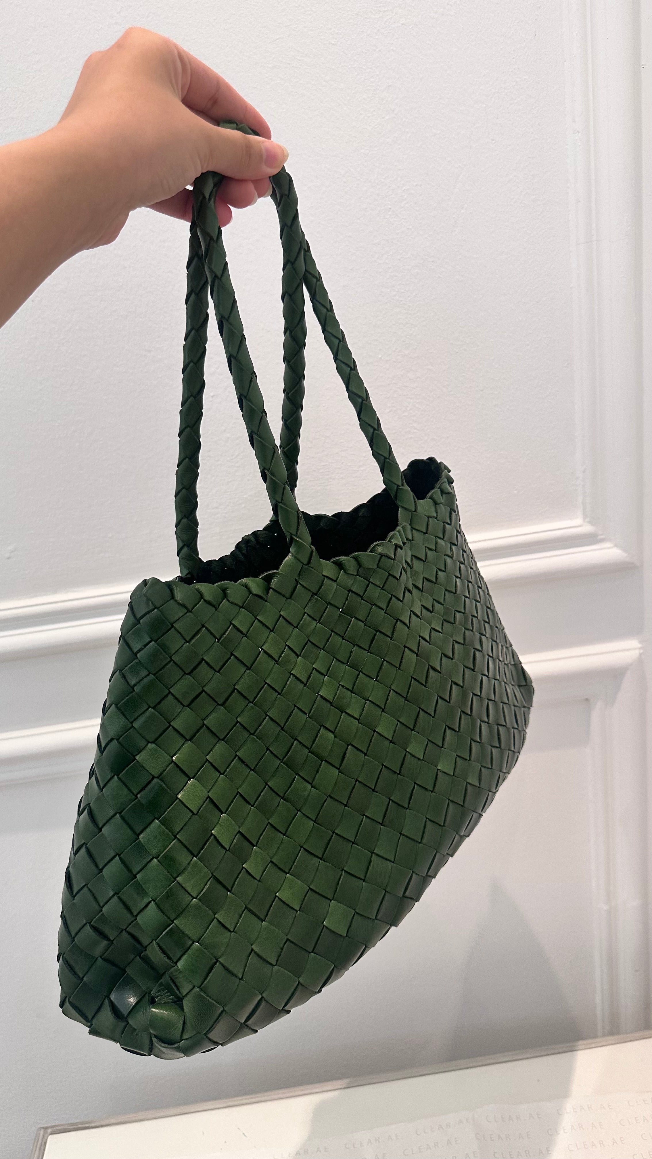 Green woven handbag held by a hand against a white background