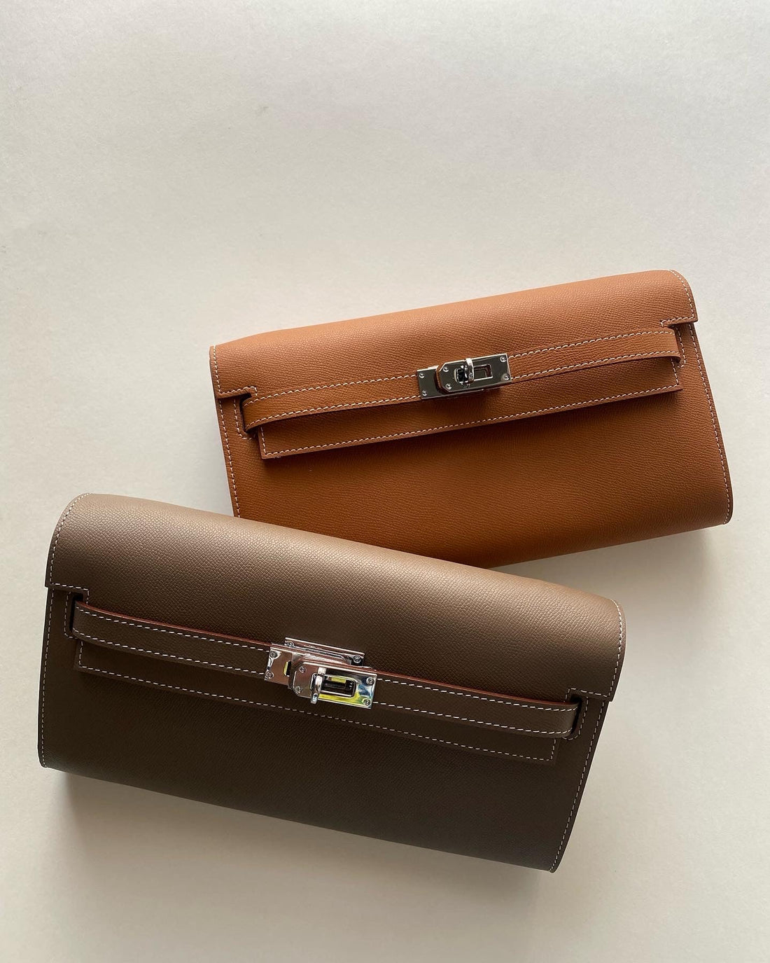 Two brown leather handbags with silver clasp on a light beige background