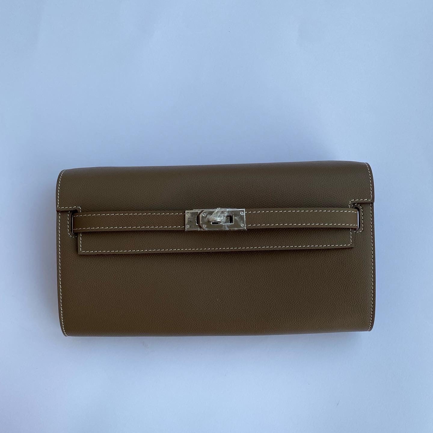 Brown leather clutch bag with a silver clasp on a light blue background