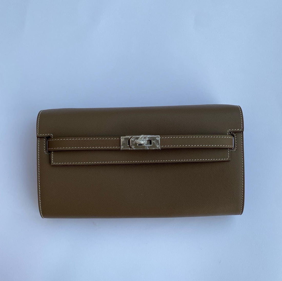 Brown leather clutch bag with a silver clasp on a light blue background