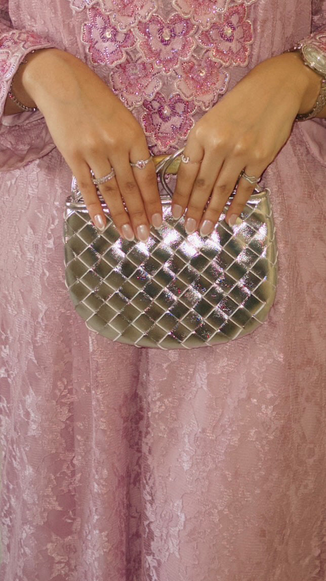 Silver woven handbag held by a person wearing a pink floral dress.