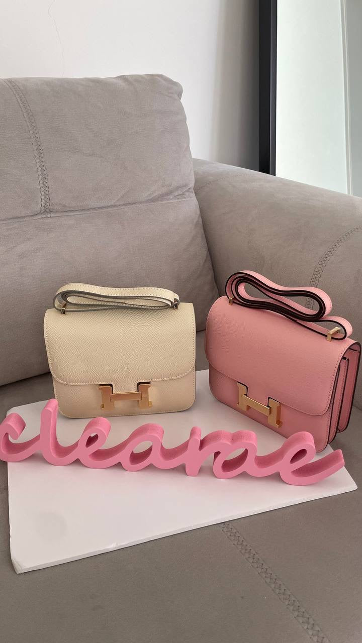 Two handbags, one beige and one pink, on a stand with a couch in the background.