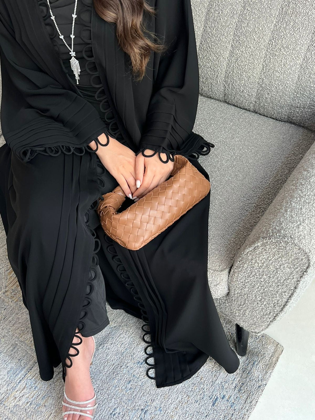 Person wearing a black outfit with a brown clutch sitting on a gray couch.