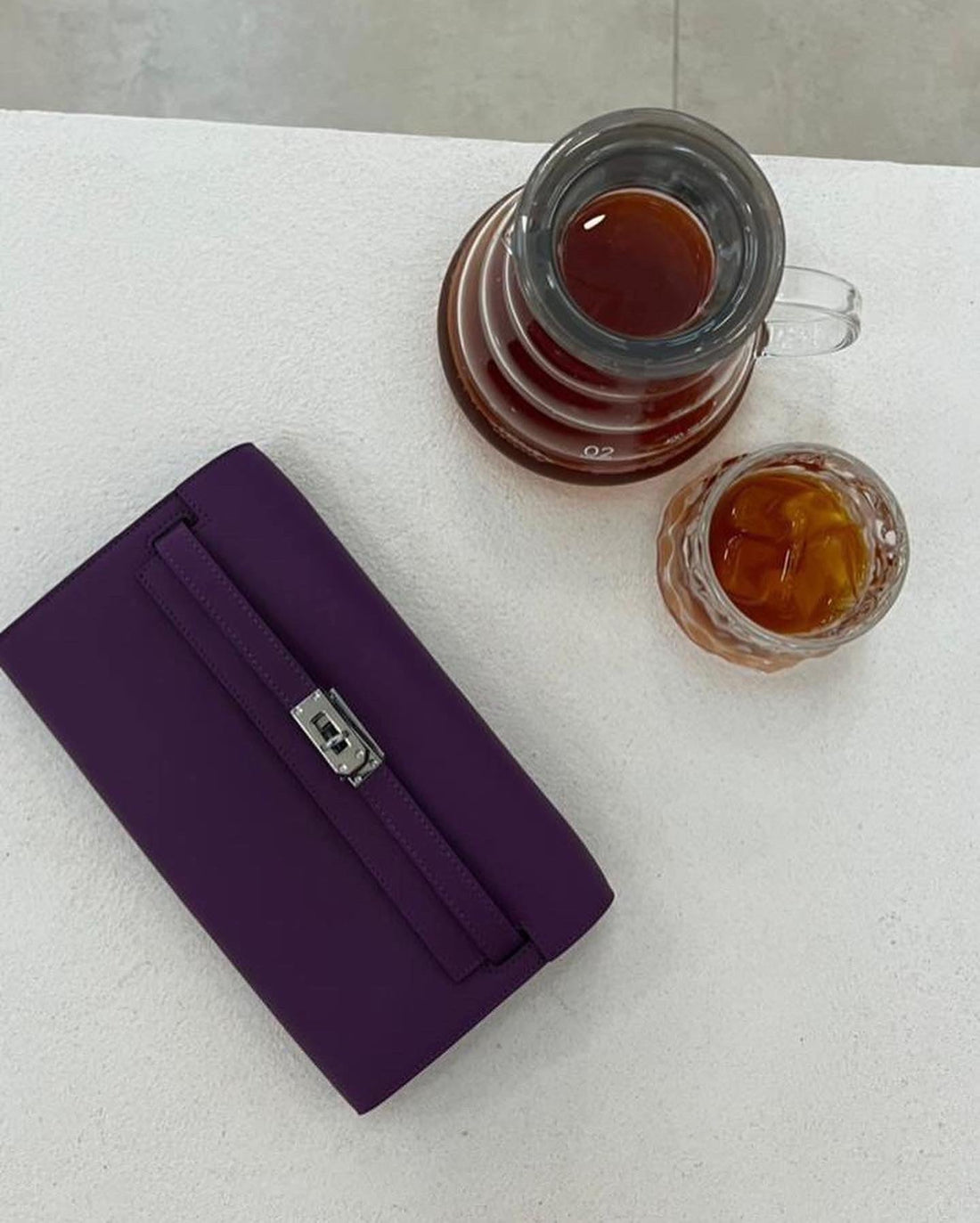 Purple wallet next to two cups of tea on a white surface