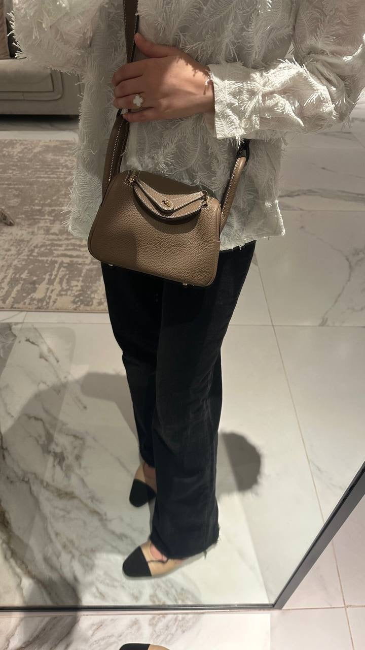 A person holding a beige colored leather handbag with a compact design.