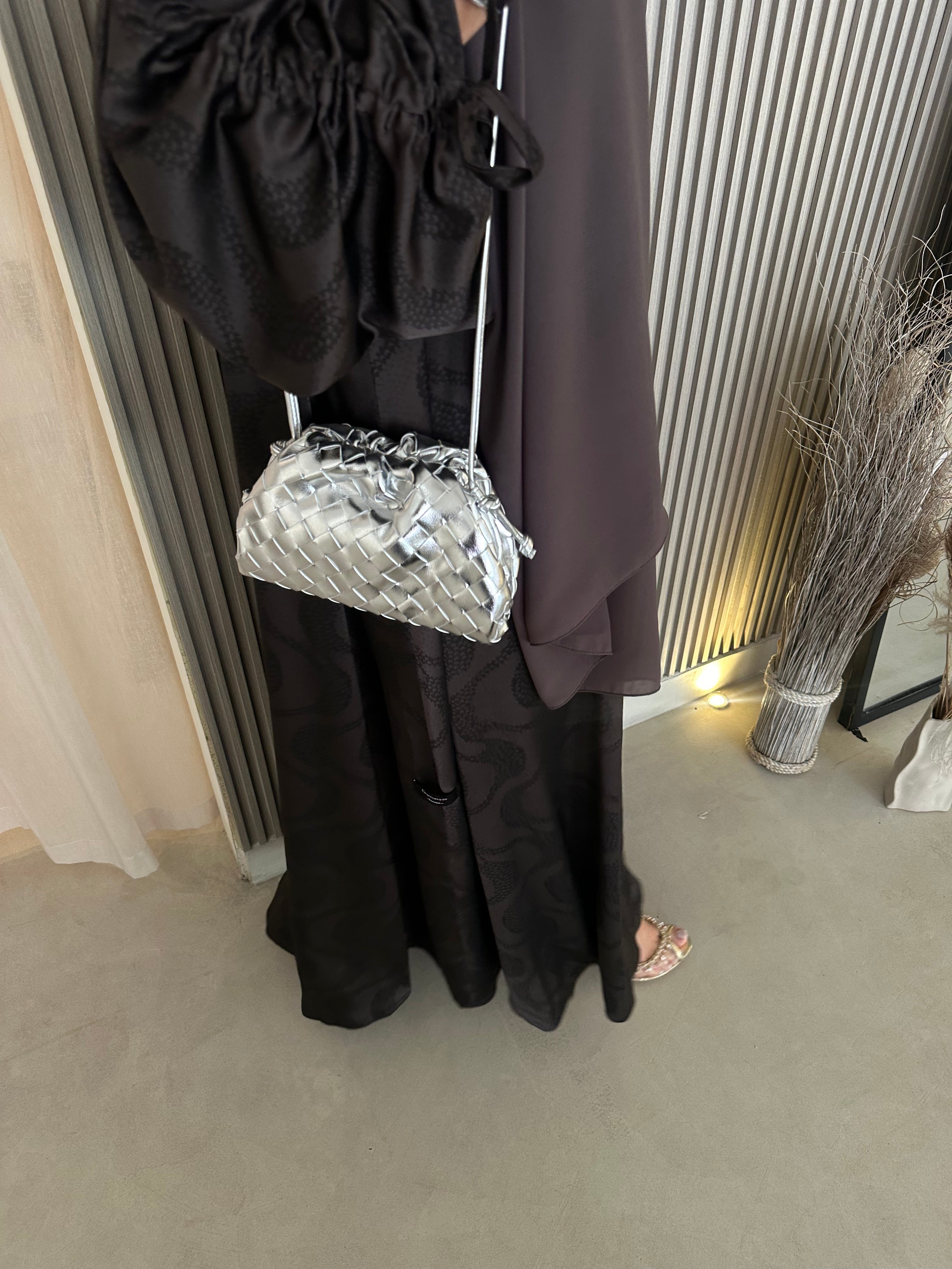 A person wearing a black outfit holding a silver, medium-sized handbag.