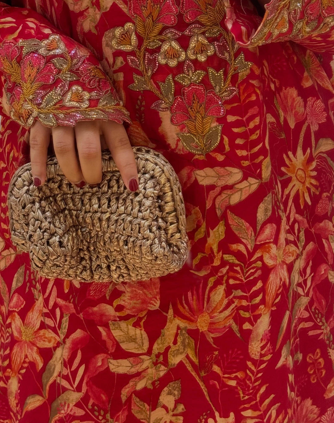 Person wearing a red floral dress holding a woven clutch.