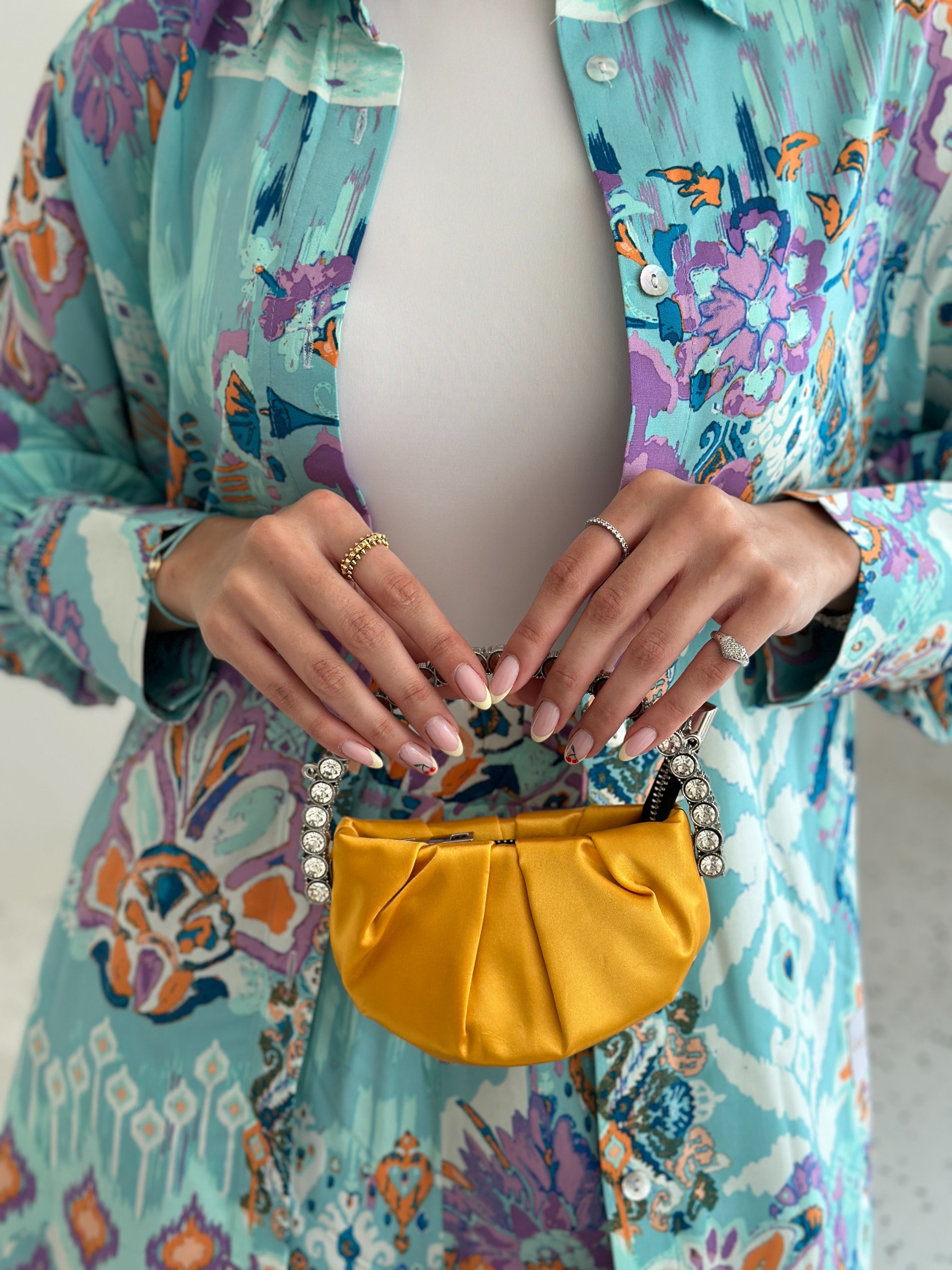 A person wearing a floral patterned shirt holding a small yellow bag with a long chain.