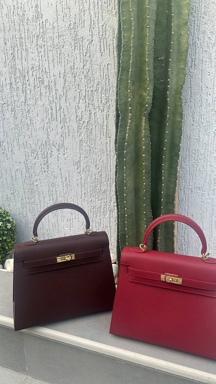 Two handbags, one brown and one red, on a surface with a textured wall and cactus in the background.