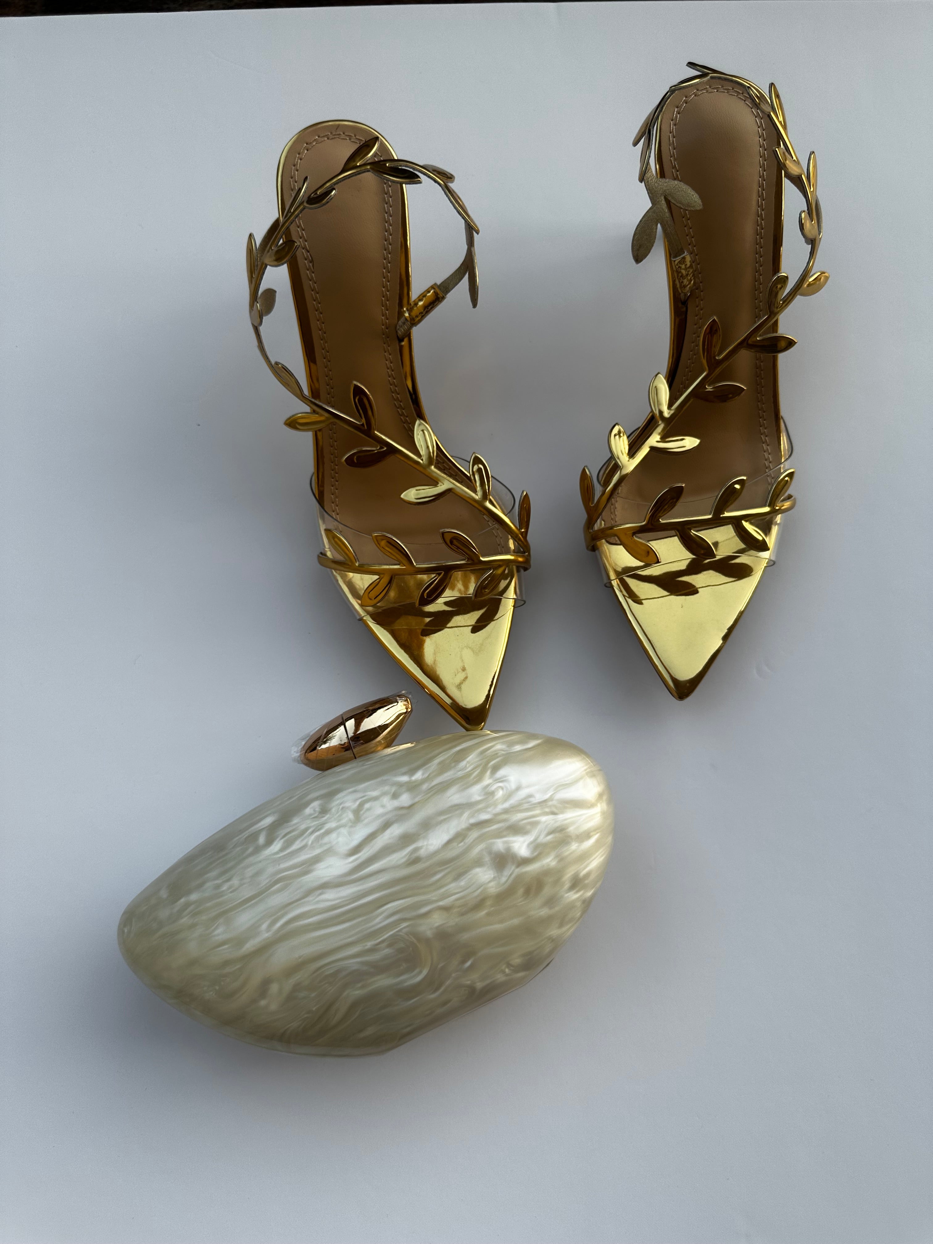 Pair of gold high-heeled shoes with leaf designs on a white background