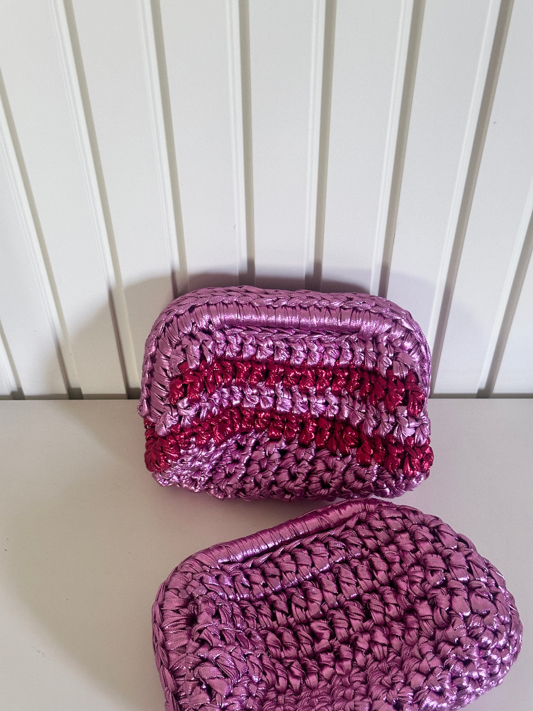Two pink crocheted pouches on a white surface with a white wooden background