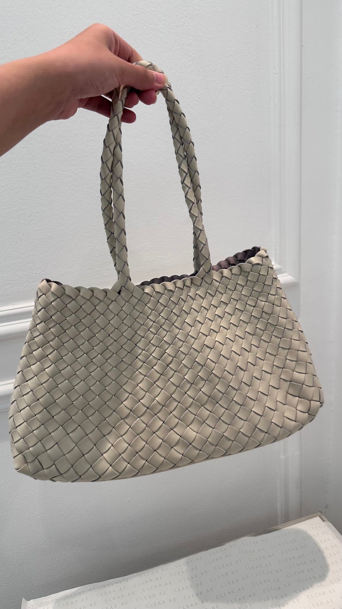 Hand holding a woven beige handbag against a plain background