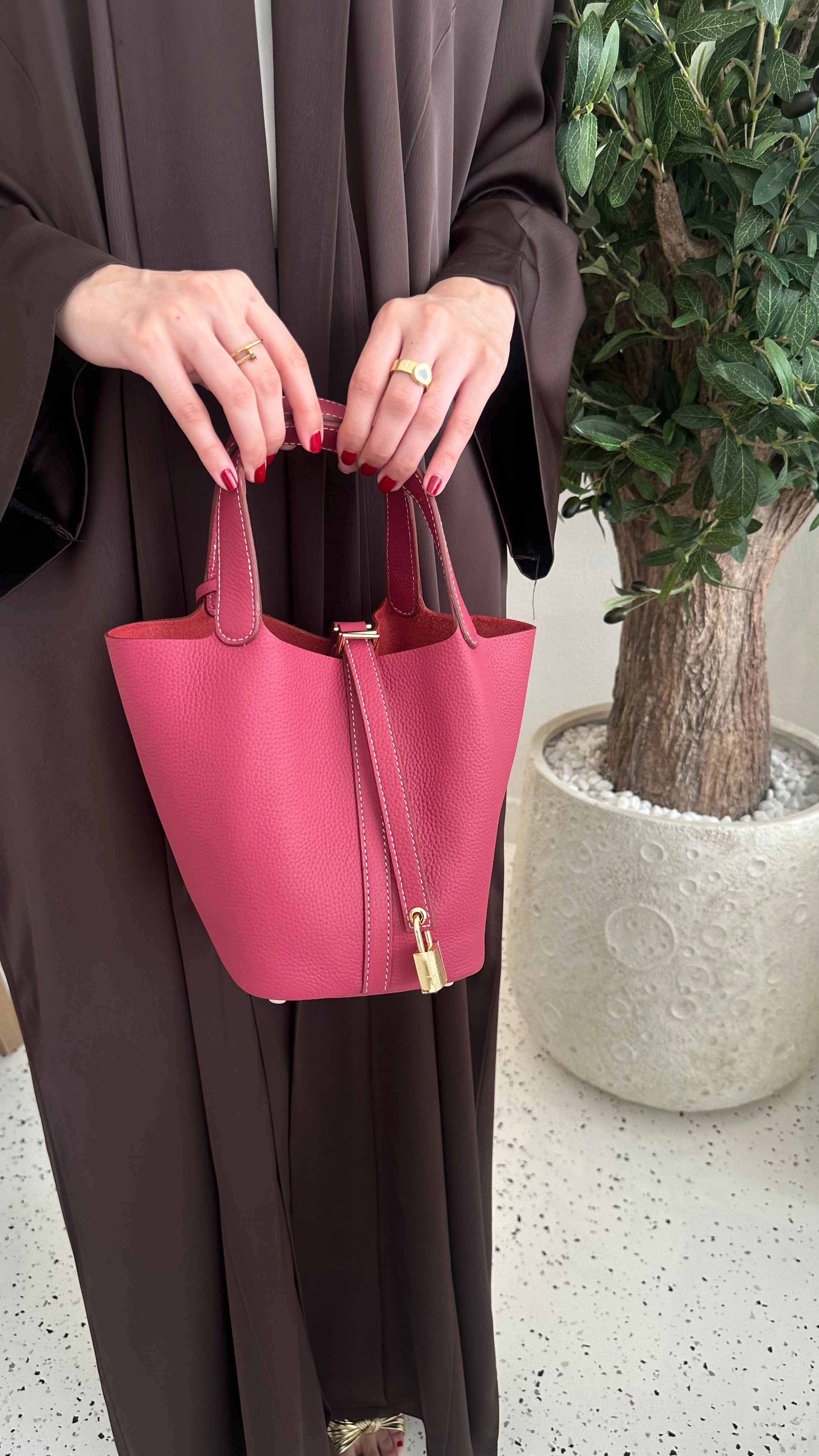 A person holding a fuchsia-colored handbag with an adjustable tab padlock in gold finish.