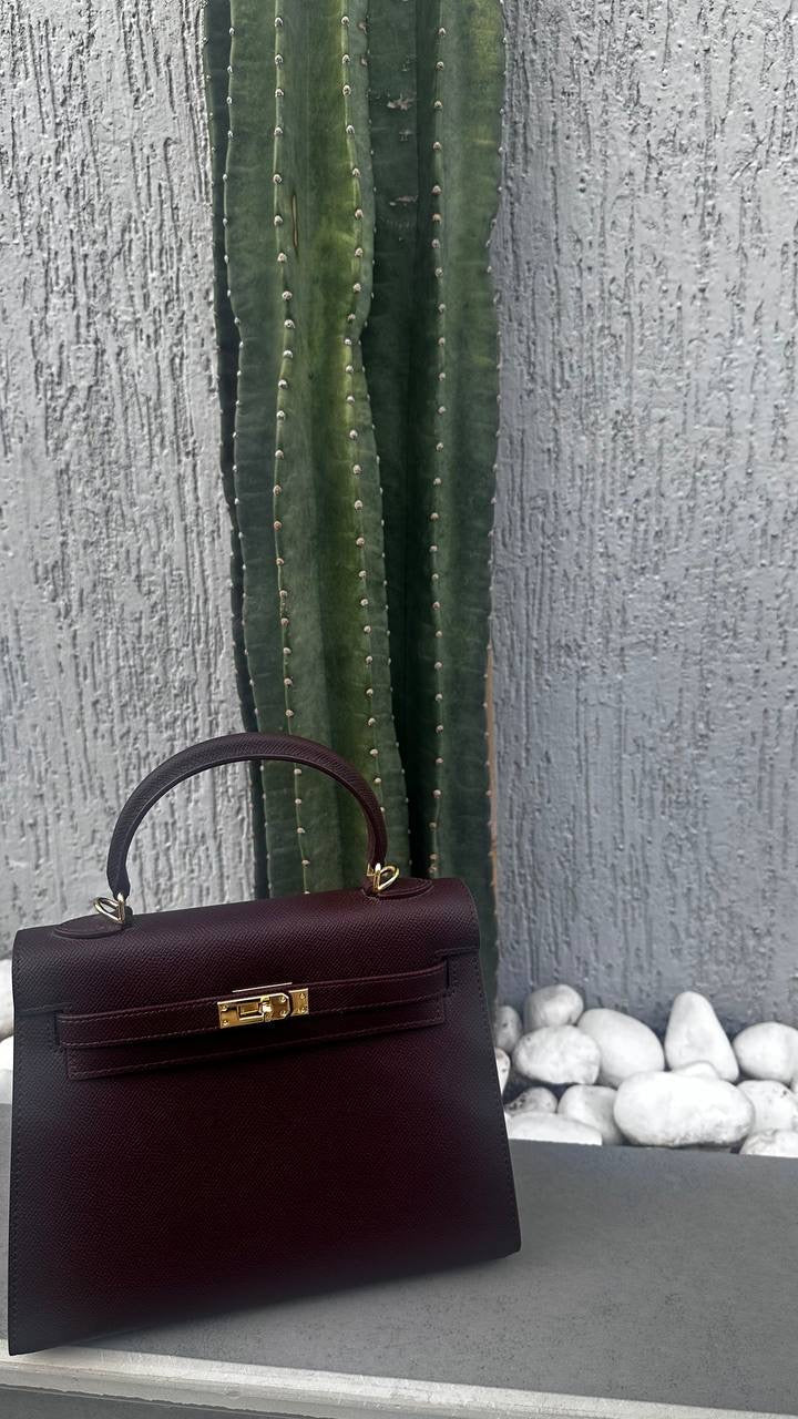 Dark brown handbag with gold hardware on a textured surface with pebbles.