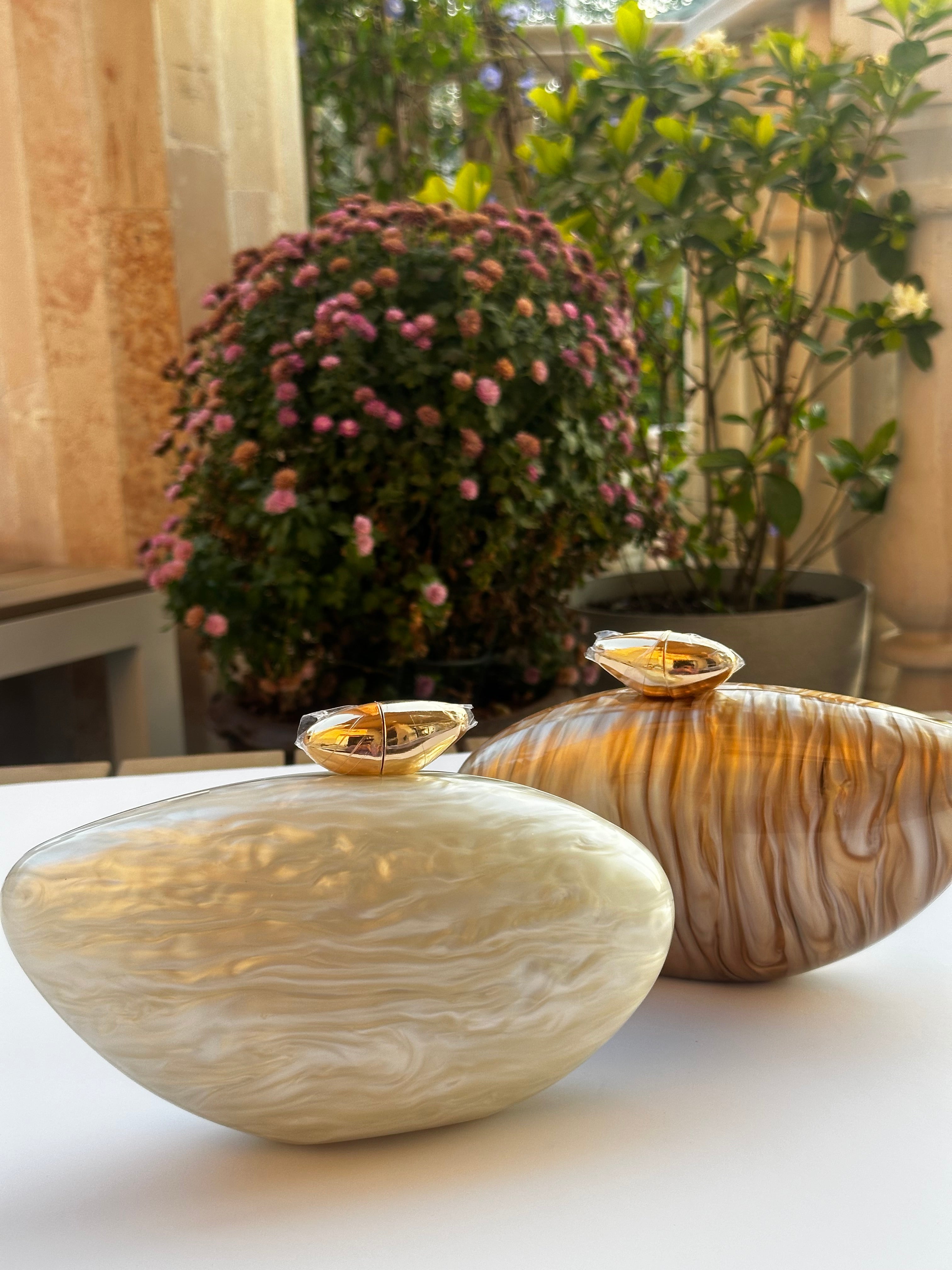 Two decorative bowls with a wavy pattern on a surface, with plants in the background.