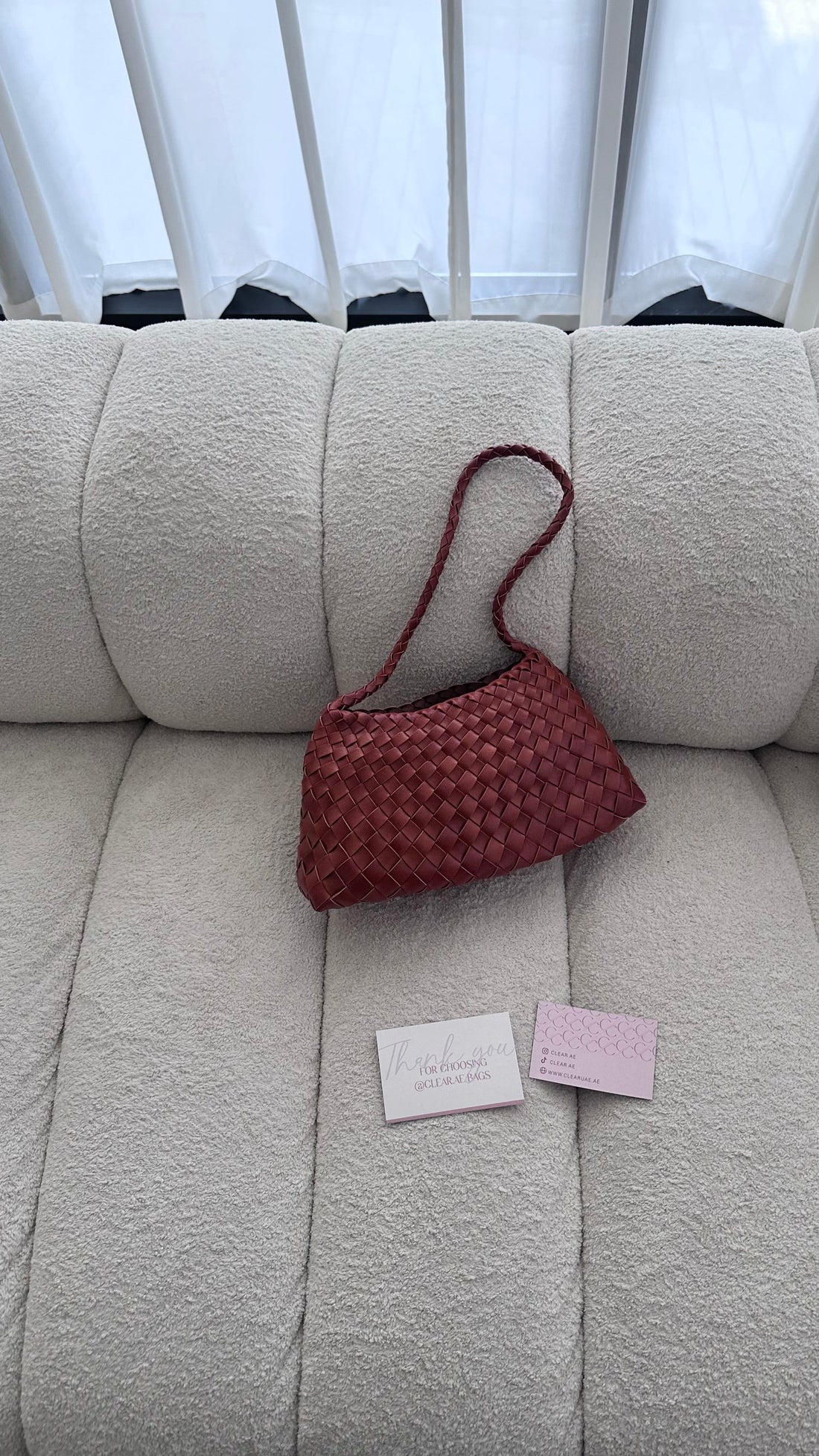 Red woven handbag on a beige sofa with a card and tag next to it.